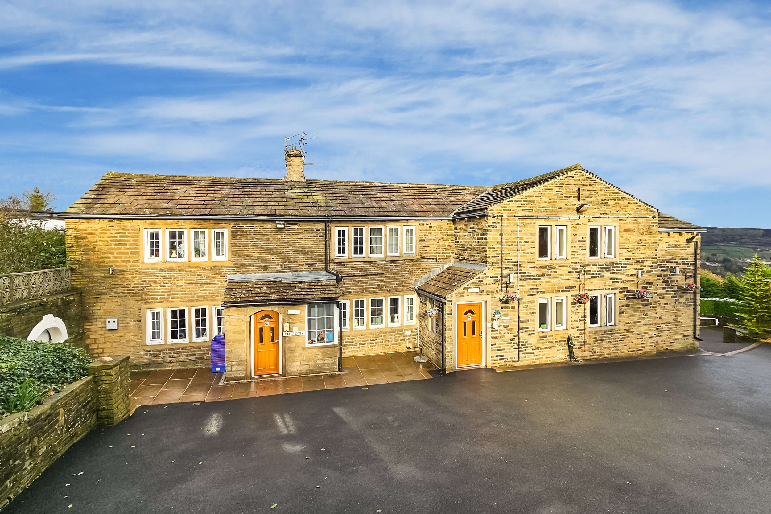 A two-story stone residential building with multiple white-framed windows and two wooden front doors, set against a bright blue sky with some clouds.