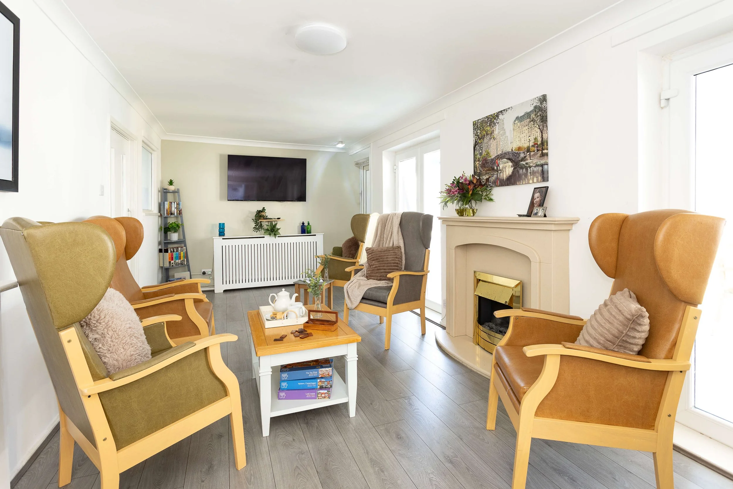 Living room with four armchairs, a fireplace, a television, a small coffee table, and various decorations, including framed pictures and plants.