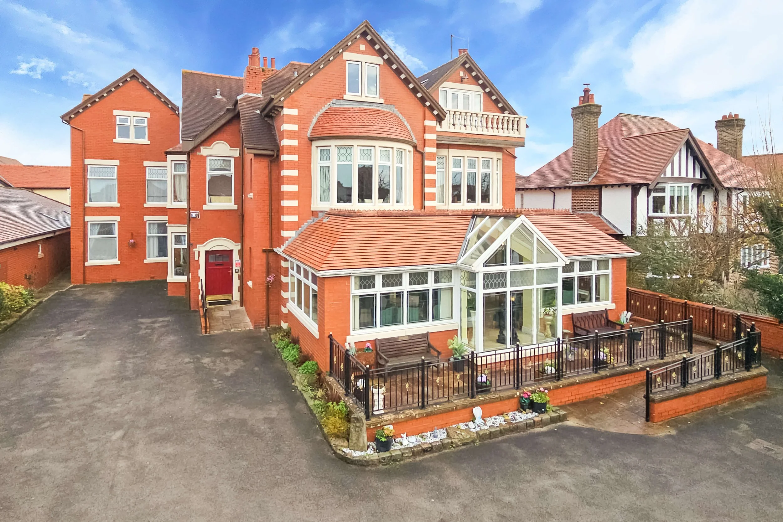 A large, multi-story red brick house with a pitched roof, multiple windows, and a front porch. The house has a glass conservatory at the ground level with a fenced outdoor patio area.