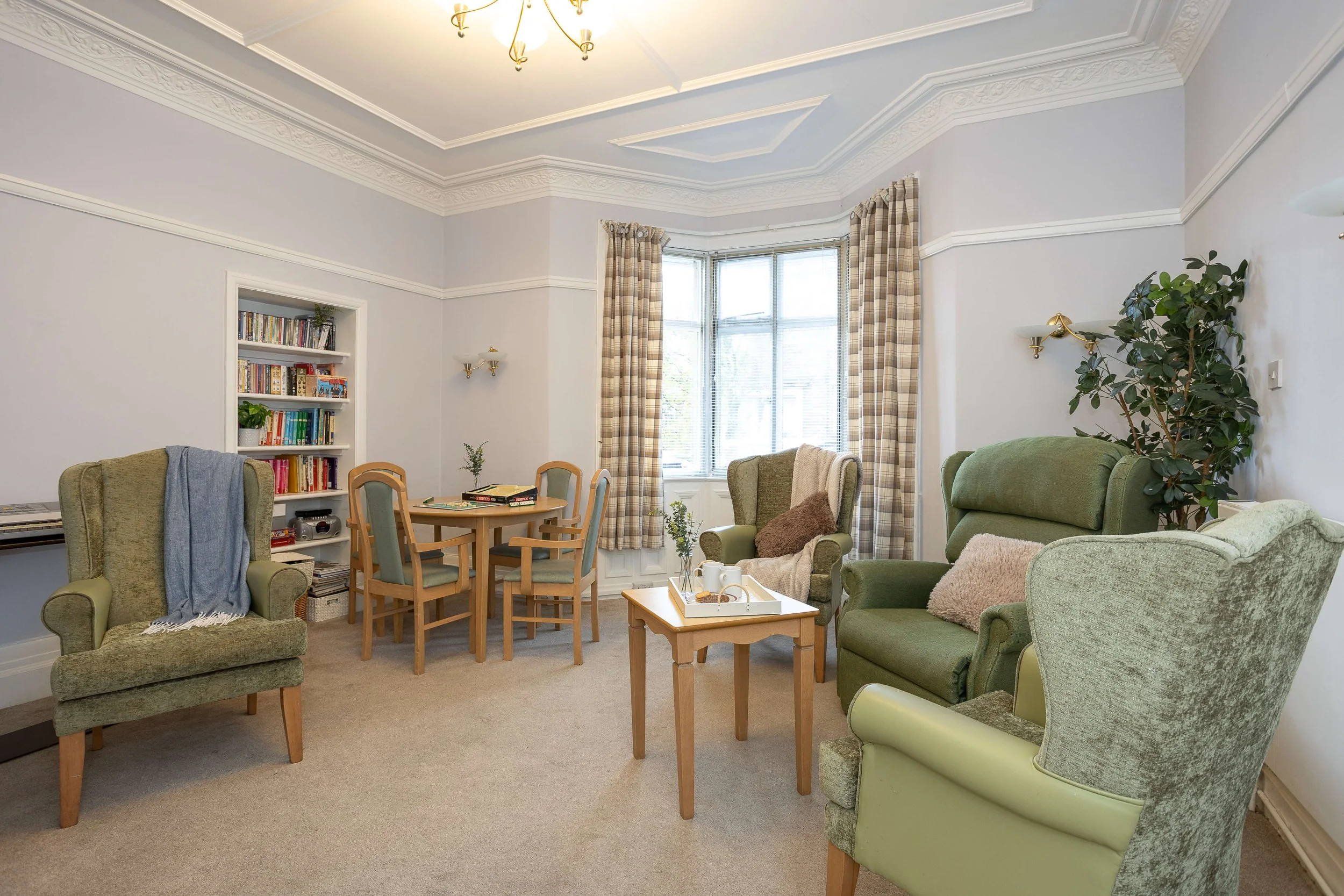 Living room with four armchairs, a round table with chairs, a bookshelf, and a window with curtains.