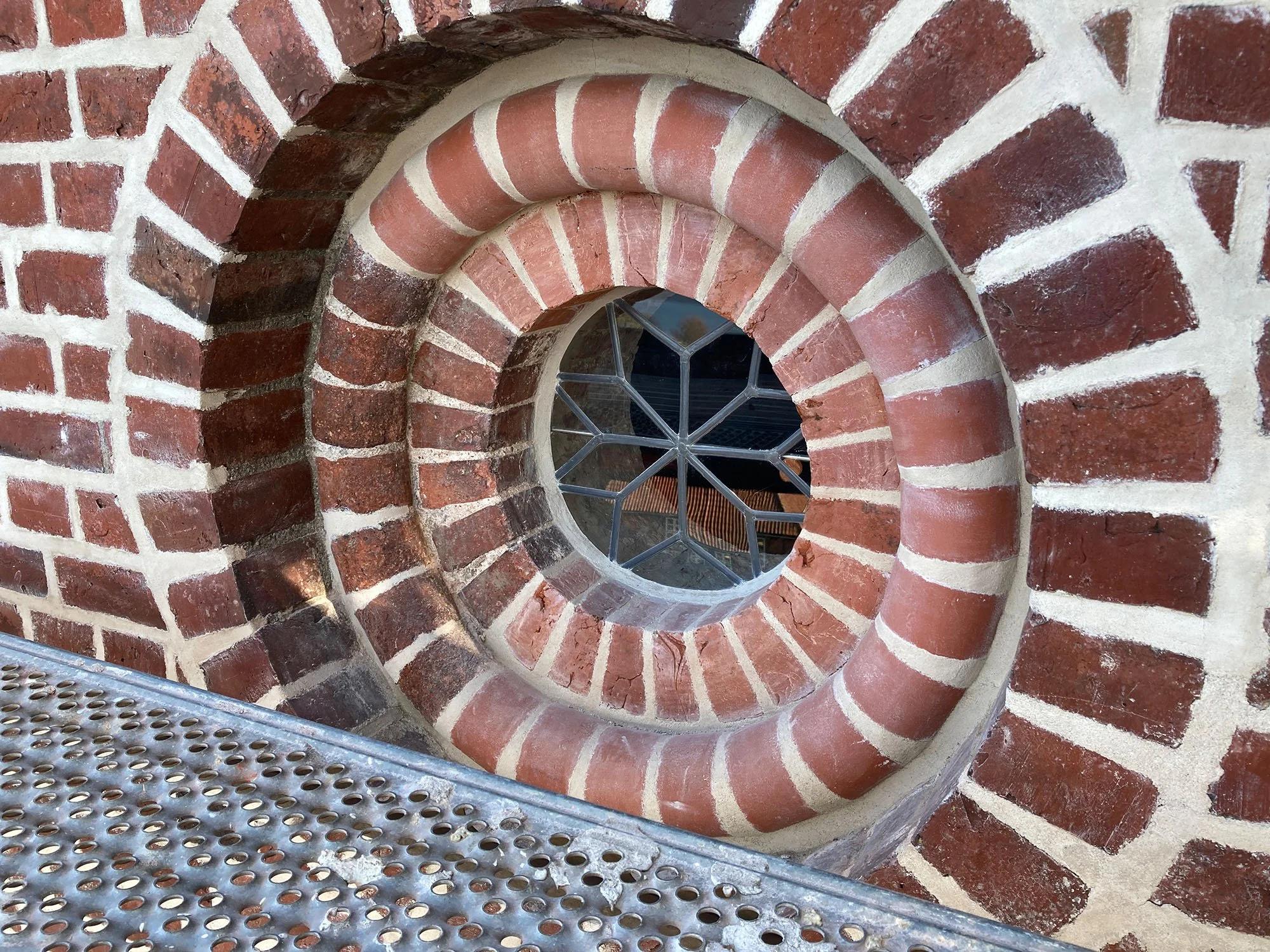Innenansicht eines spiraligen steinernen Treppenturms mit roten Ziegelsteinen und einem kleinen runden Fenster.