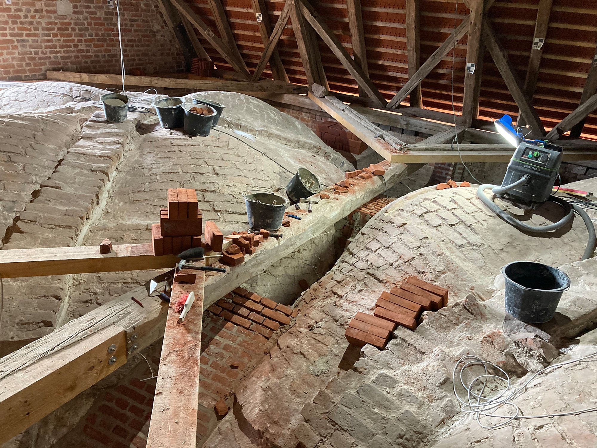 Bauarbeiten an einem alten Dach mit alten Ziegeln, Werkzeugen und Baumaterialien auf dem Dachboden.