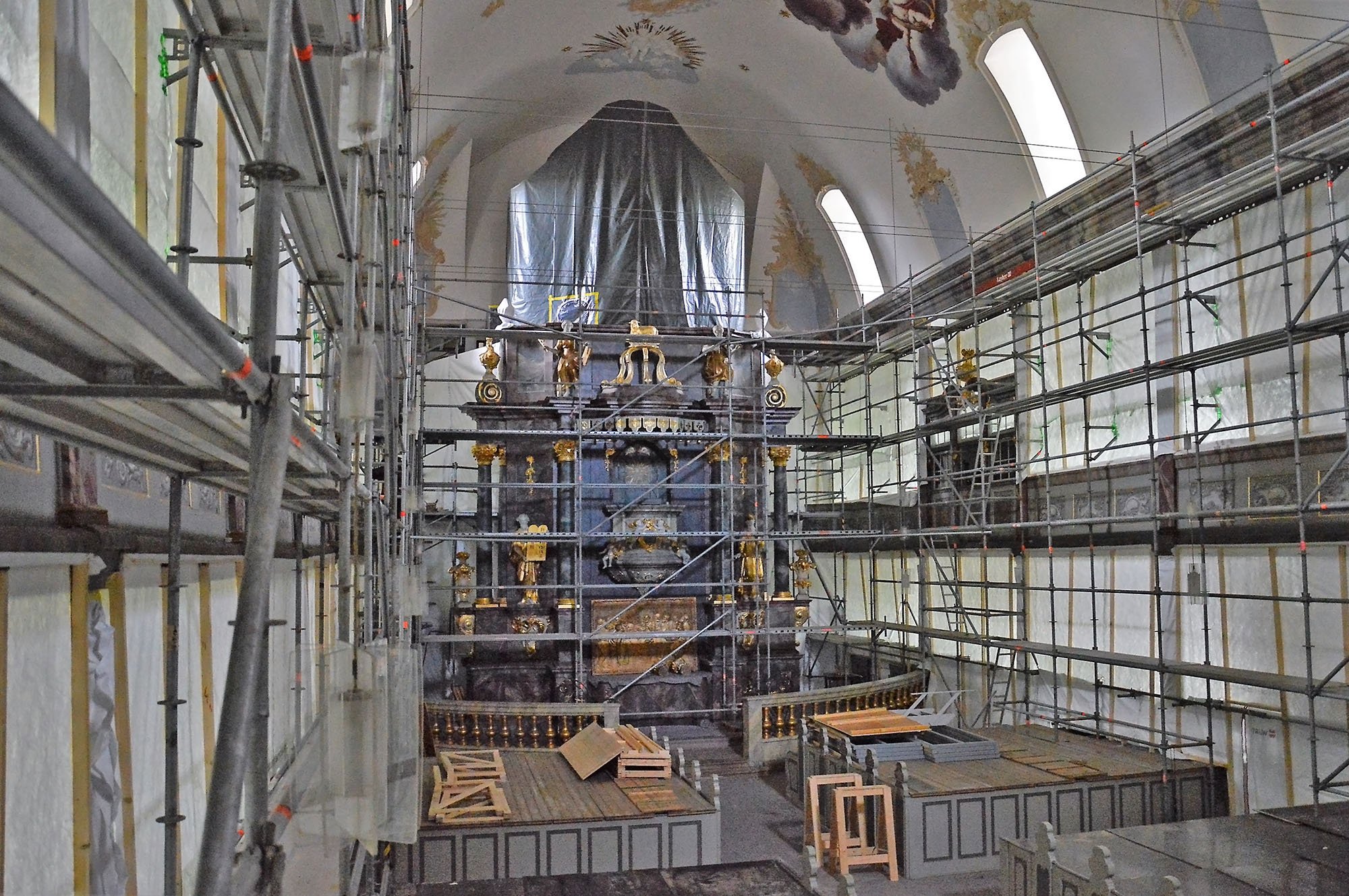 Innenansicht einer Kirche unter Renovierung mit Gerüsten, die das Altarbild und die Wandkunst schützen.