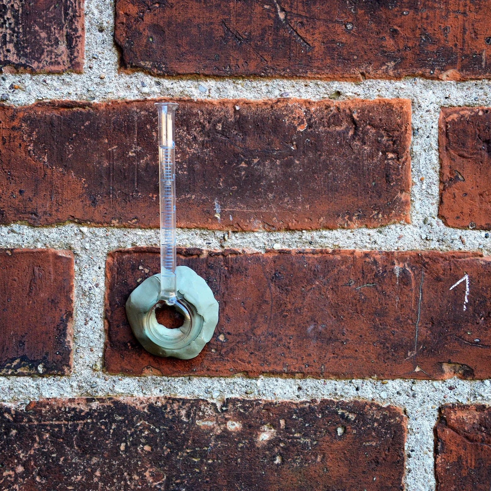 Ein Thermometer liegt auf einer Mauer aus roten Ziegelsteinen.