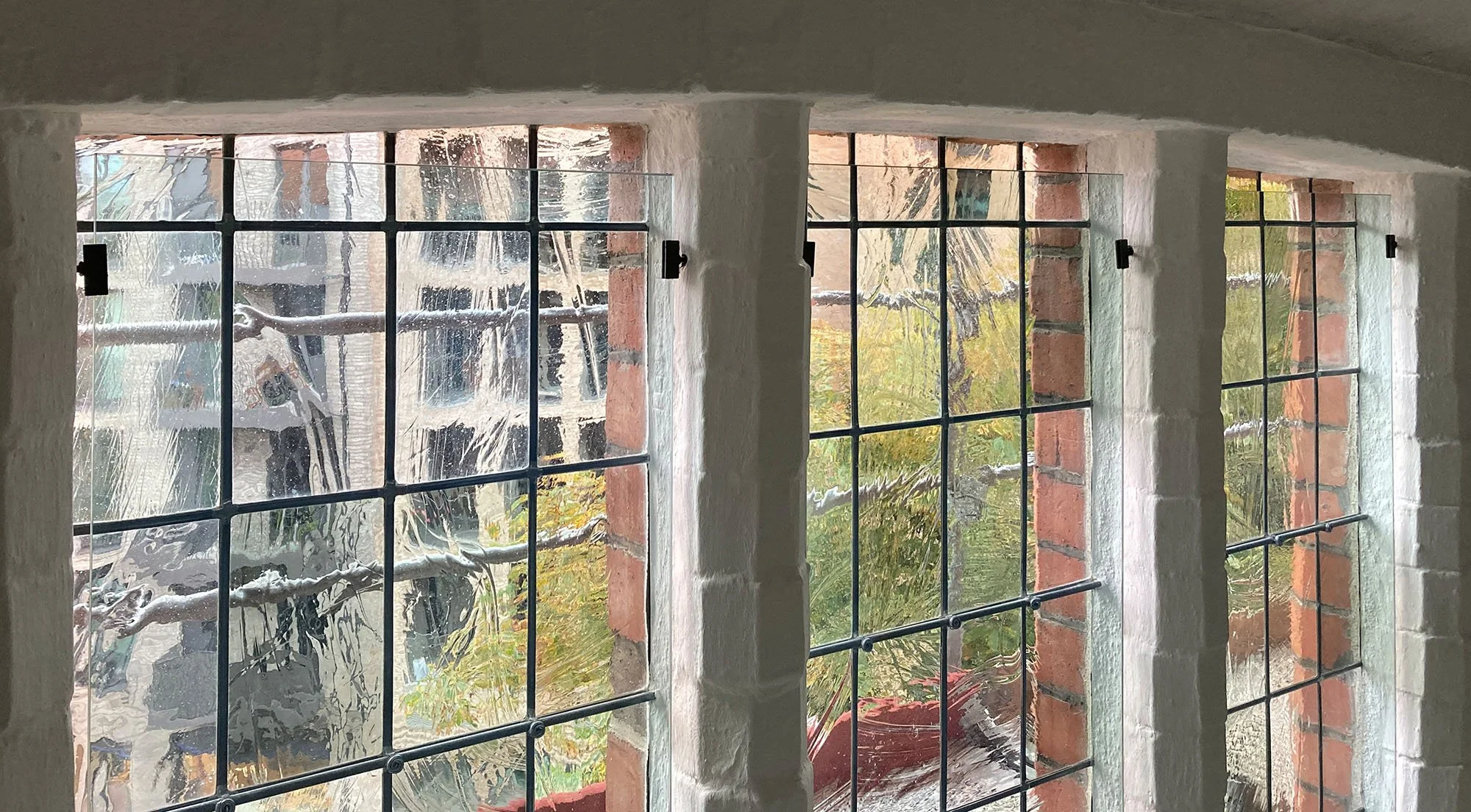 Fenster mit Metallgittern in einem Gebäude, Blick auf einen Garten mit Pflanzen und Bäumen