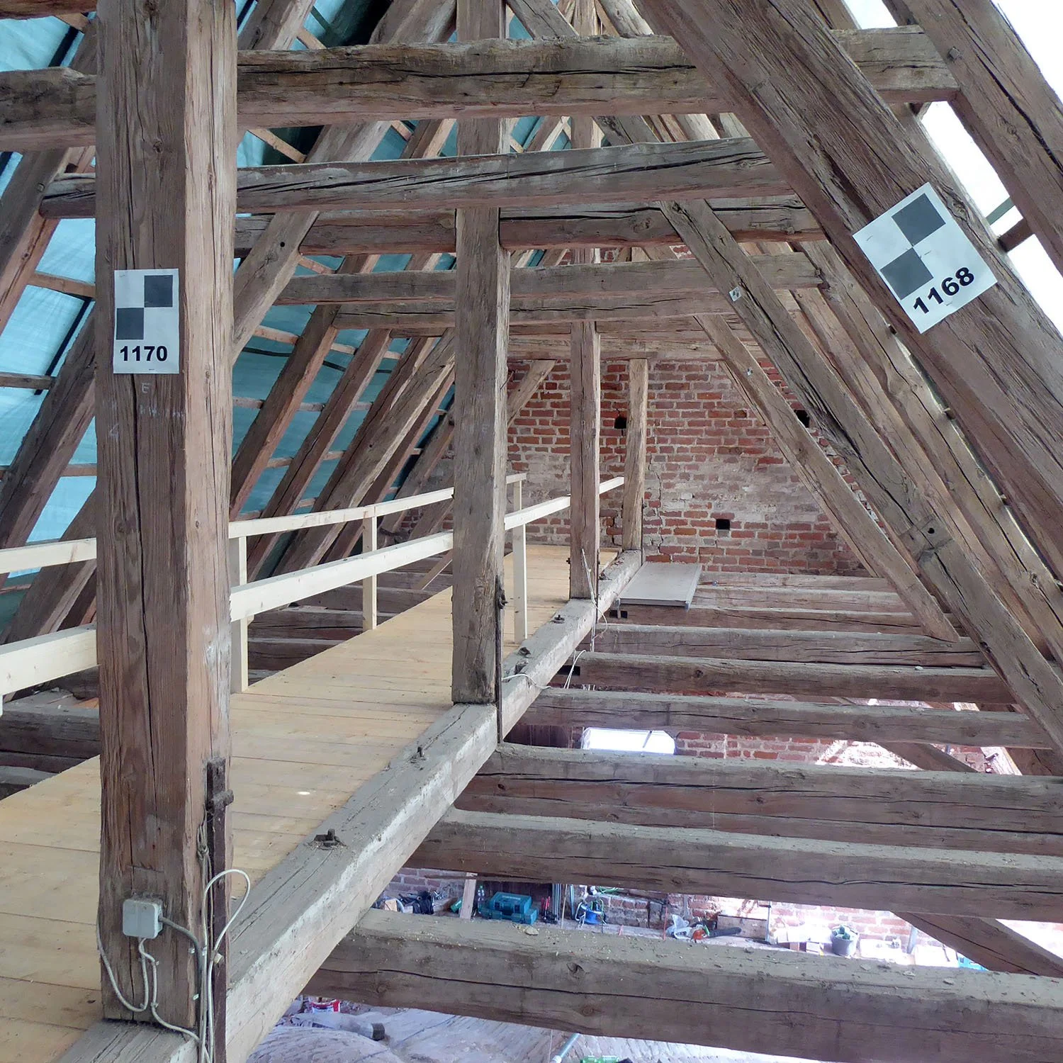 Innenansicht eines Holz- und Ziegel-Dachbodens mit Holzbalken und einer provisorischen Holzbrüstung.