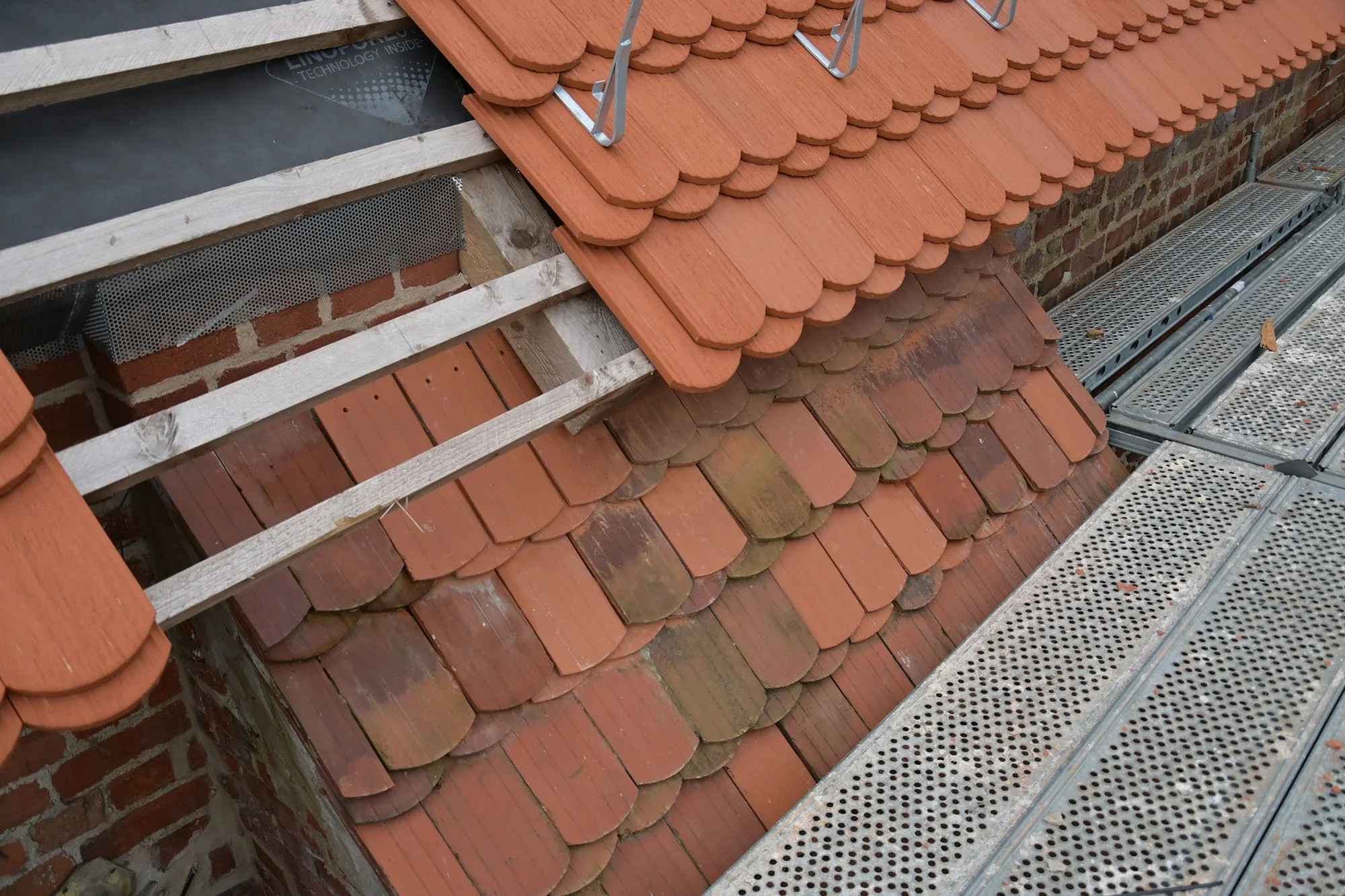 Ein Dach mit roten dachziegeln und nebendran eine Baustelle mit Metallgerüst und Holzbalken.