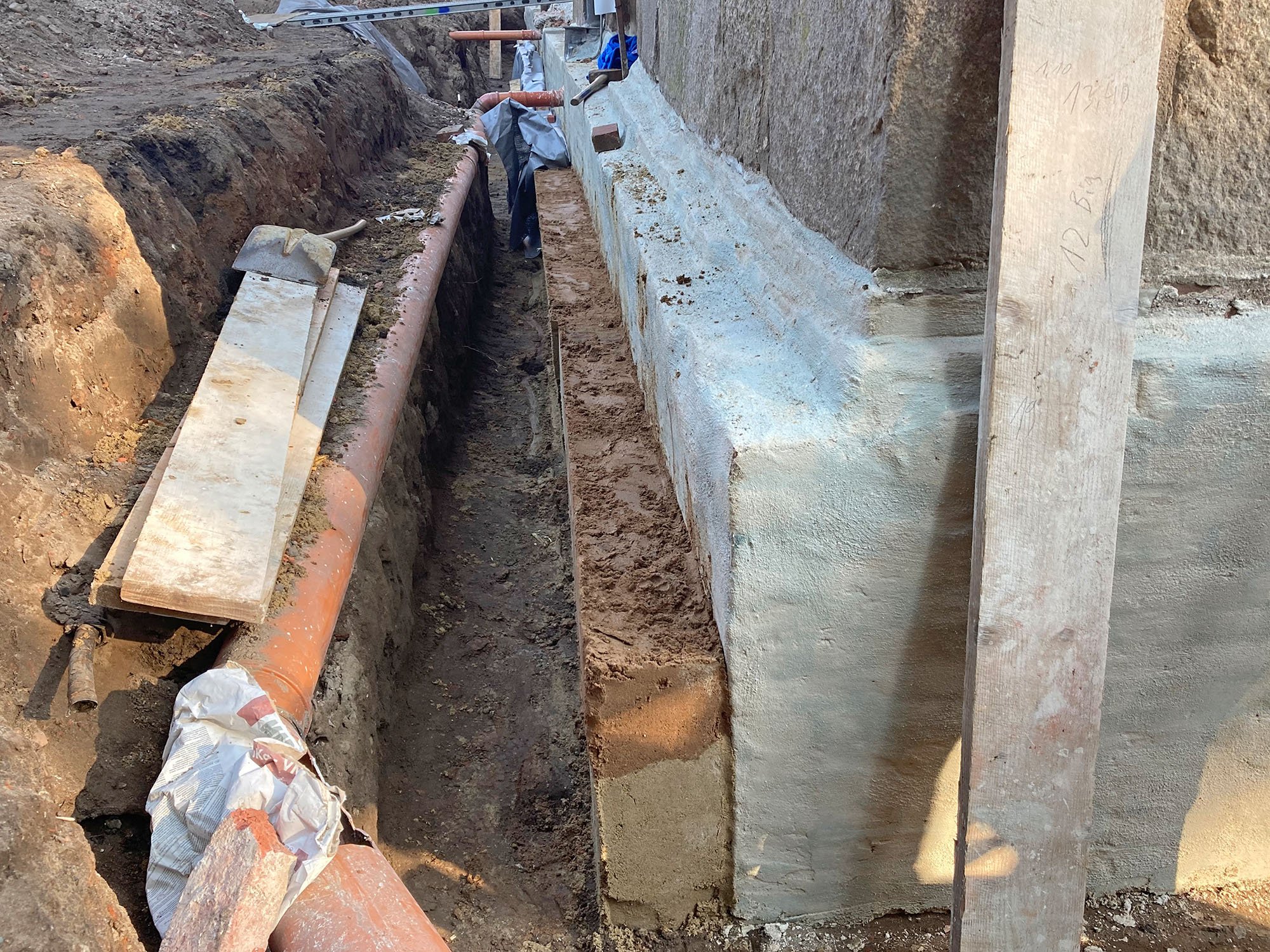 Baustelle mit Rohren, Betonwand und Baustemmen.