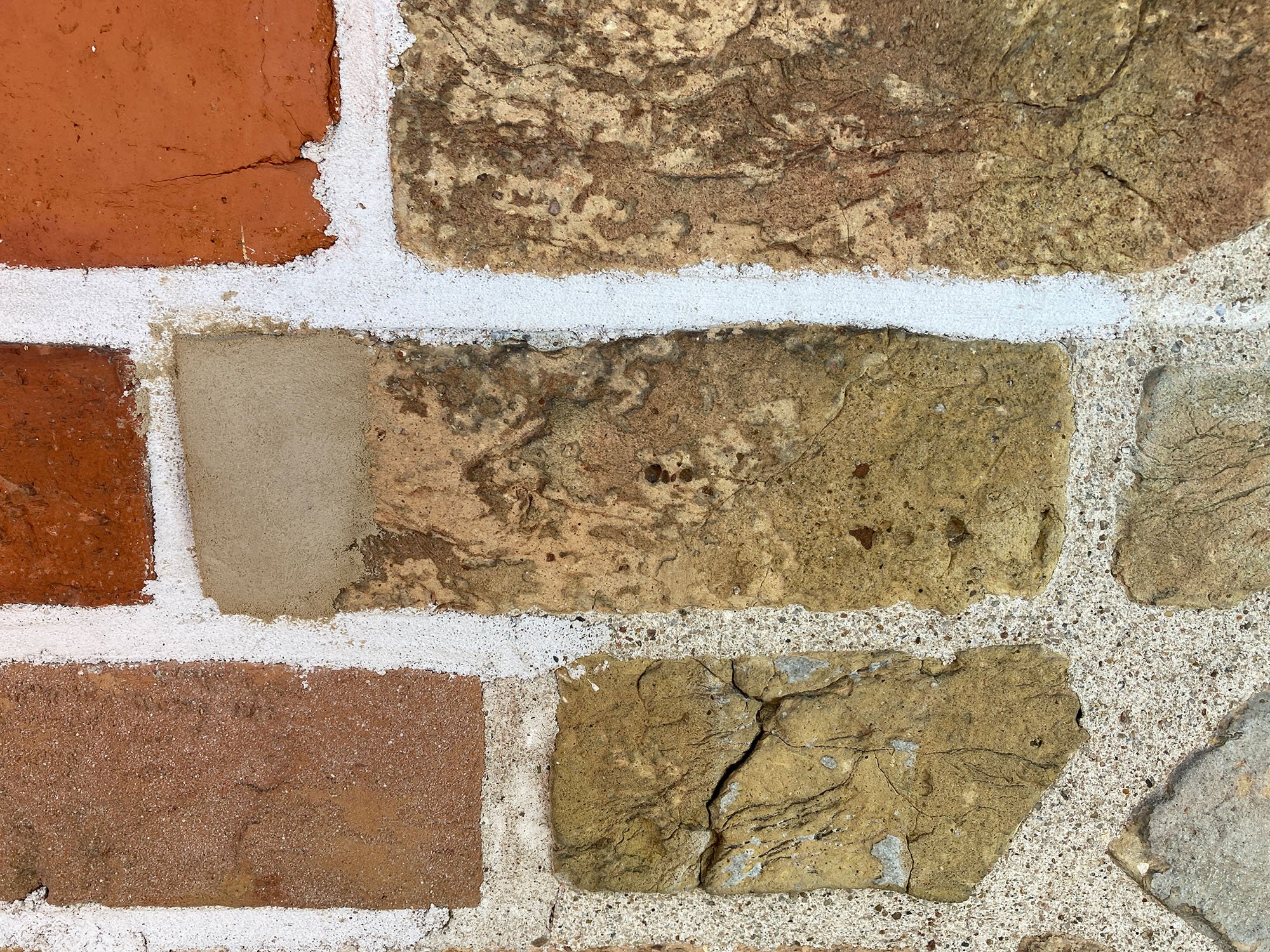 Nahaufnahme einer Mauer mit Ziegelsteinen und Natursteinen, die mit weißen Mörtel verbunden sind.