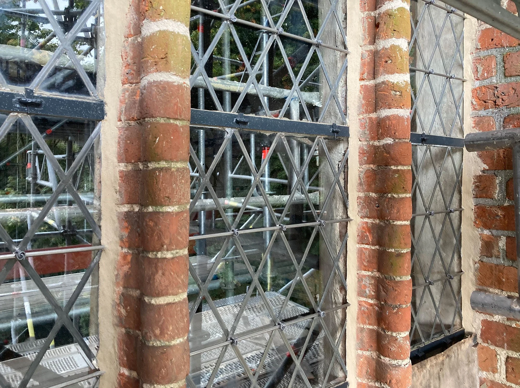 Baustelle mit Stahlrahmen, Gitter, und Ziegelmauer, vermutlich Fensterrekonstruktion oder Sanierung.