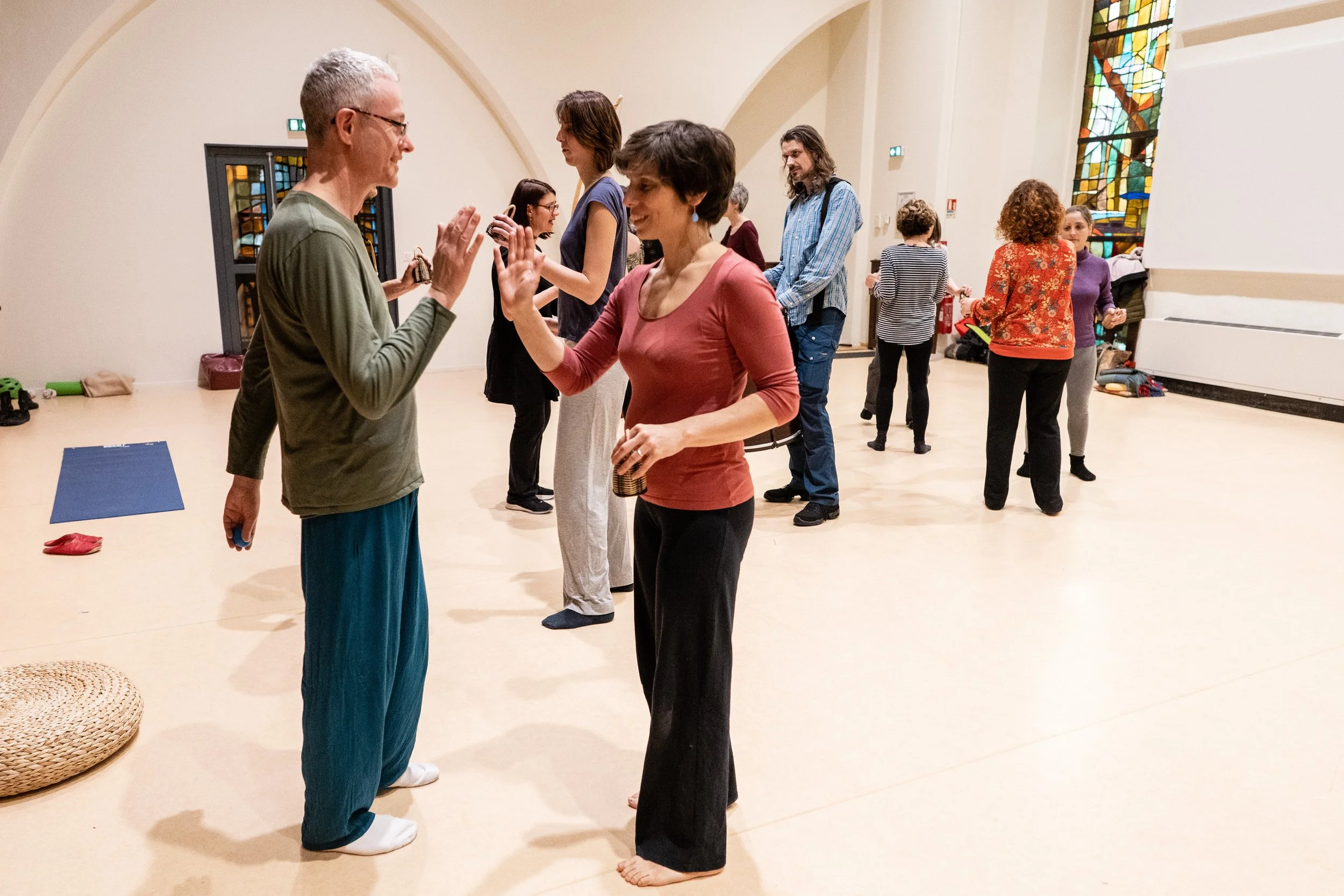 Groupe de personnes dansant dans une salle de pratique danse, avec des vitraux colorés en arrière-plan.