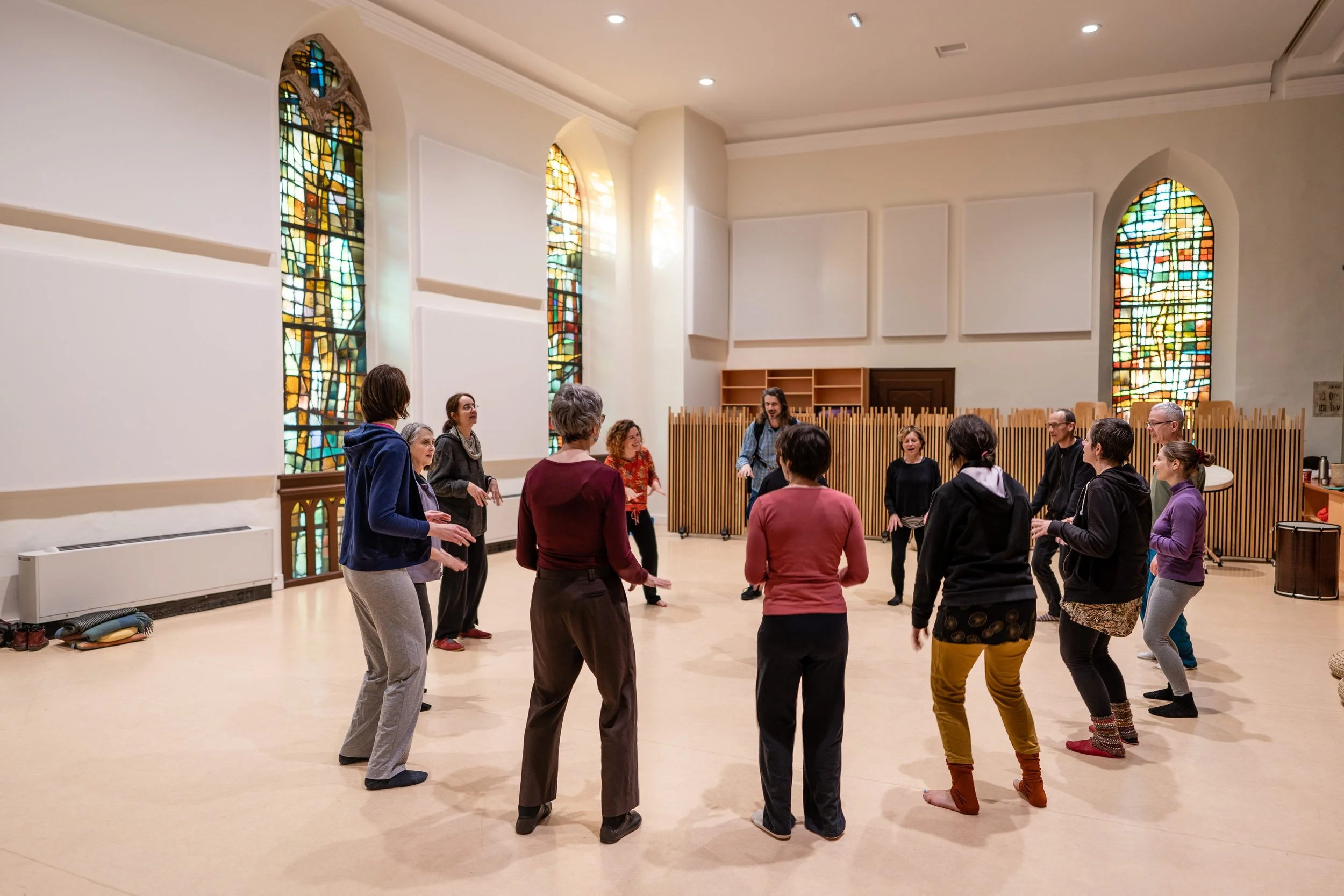 Groupe de personnes âgées participant à une session de TaKeTiNa dans une salle avec vitraux colorés et murs blancs.