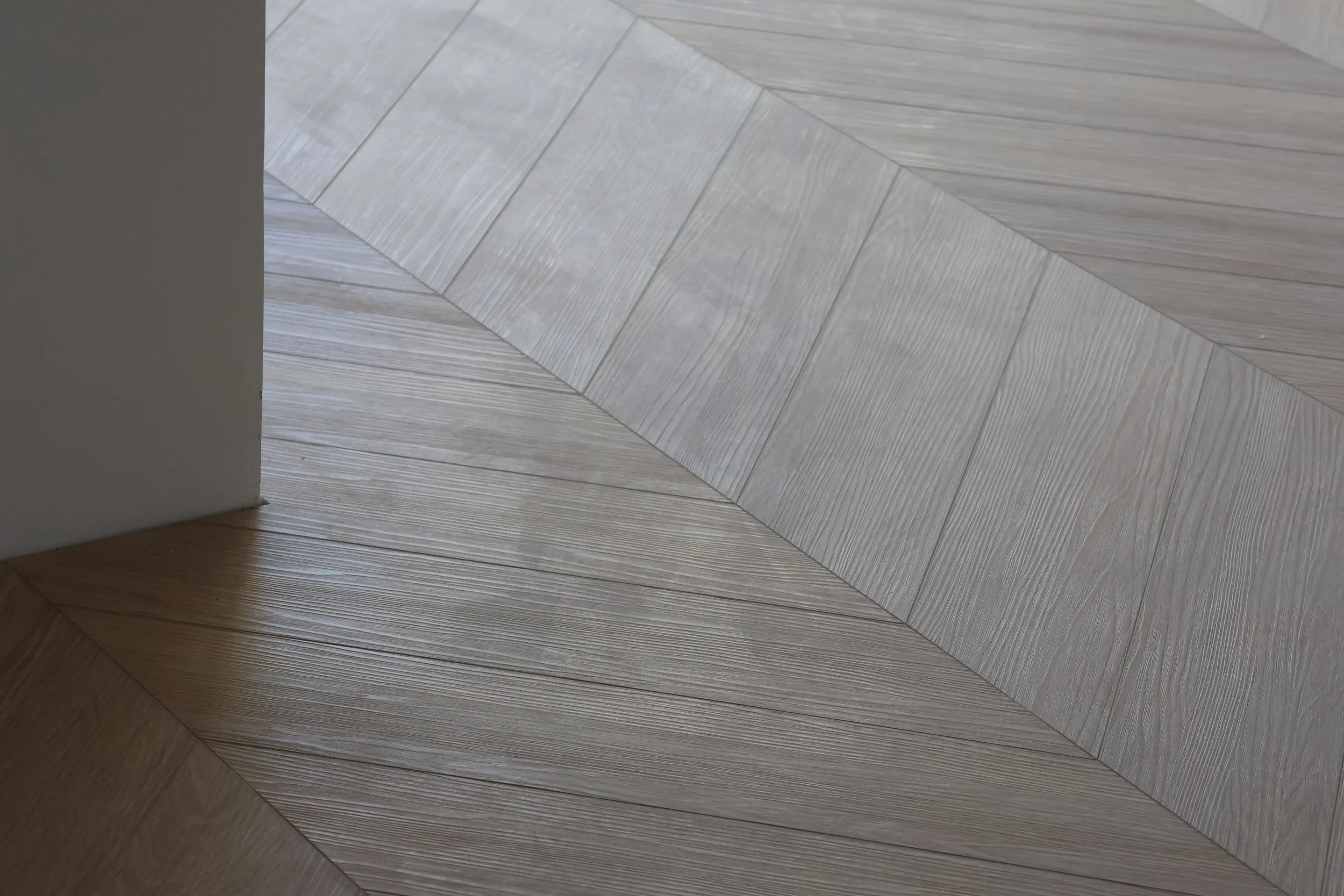 Close-up of a wooden floor with a chevron pattern, next to a white wall.