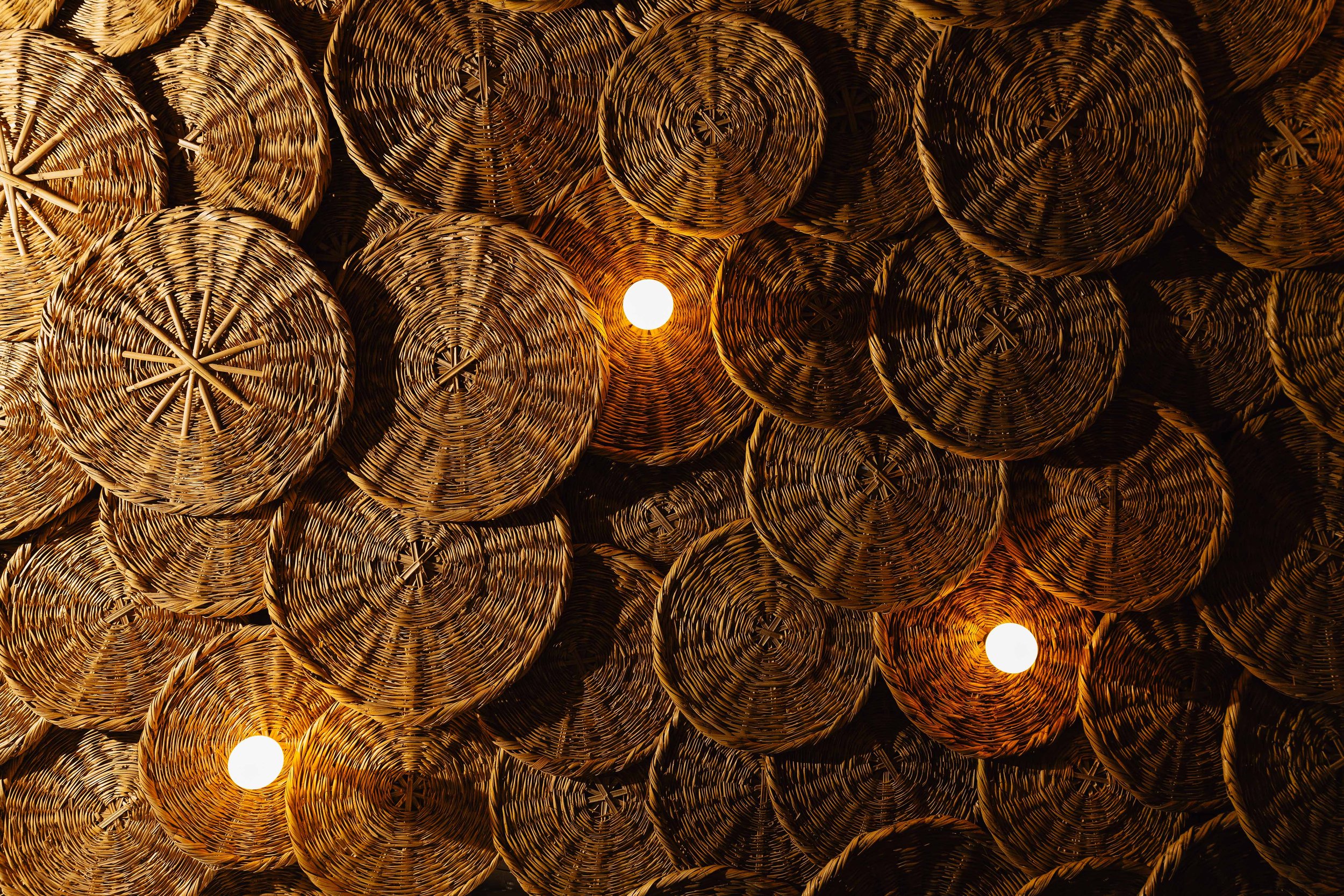 Close-up of a ceiling made of woven straw baskets with three small circular lights.