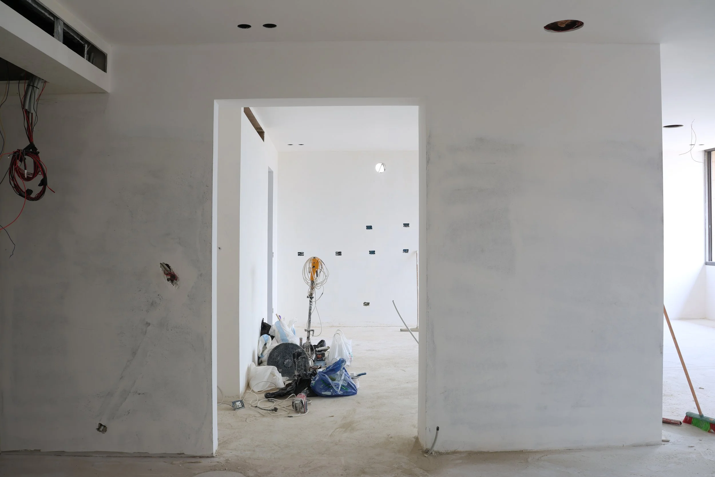 Interior of a room under construction with unfinished walls, exposed wiring, and construction tools and materials on the floor.