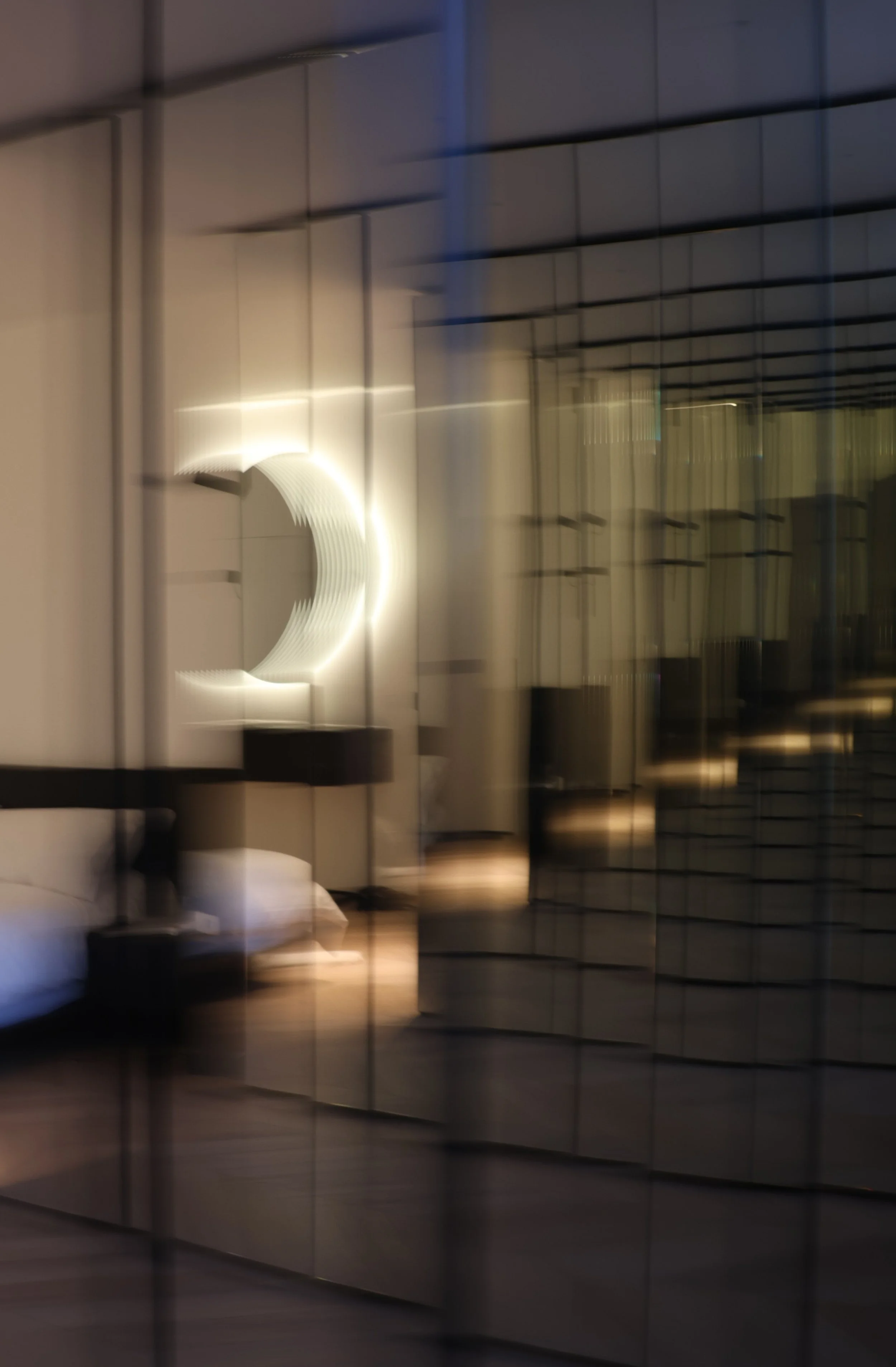A photo of a modern hotel room with a bed, mirror, and soft lighting, seen through a reflective, patterned glass window.