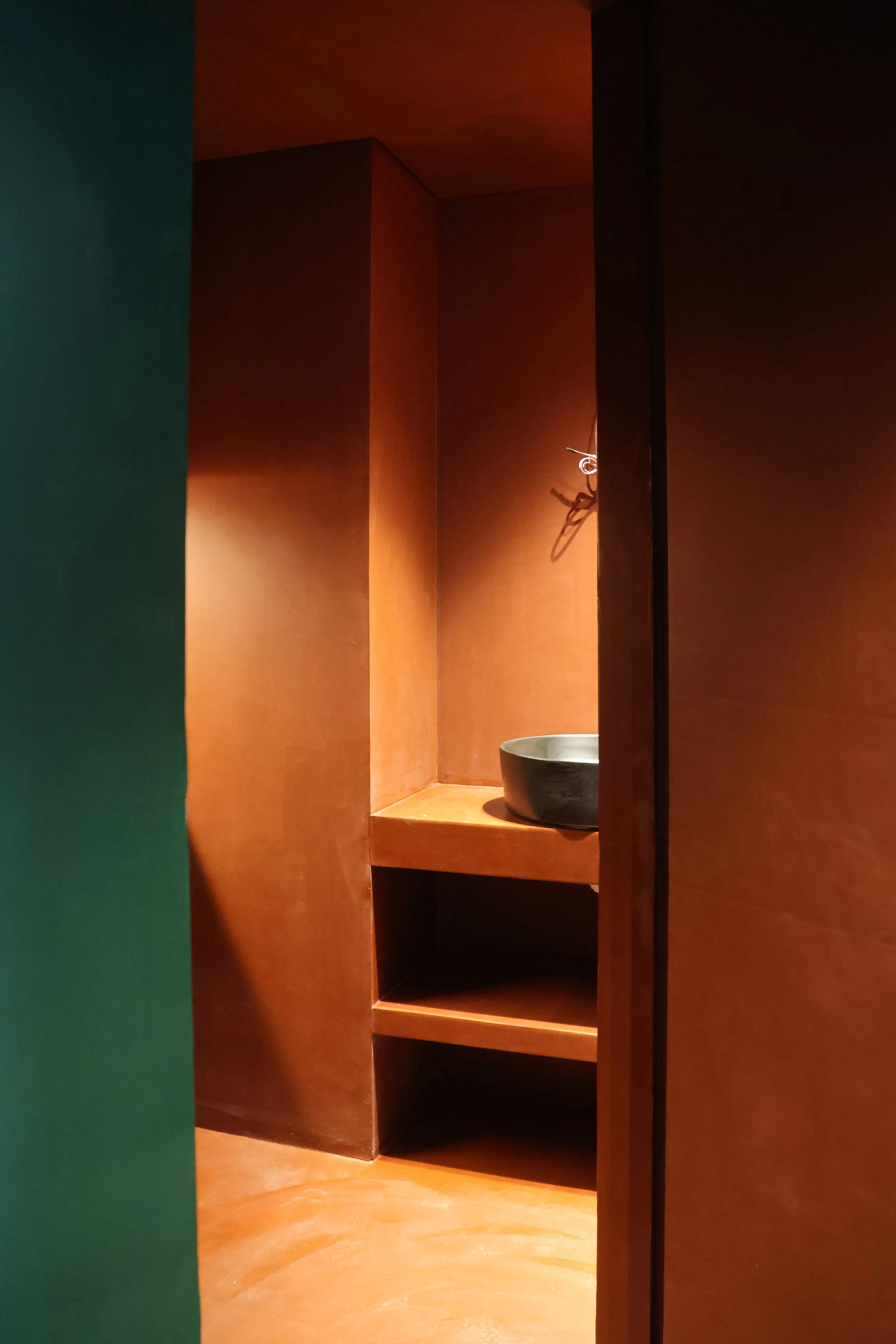 A small, dark-colored bowl on a wooden shelf inside a wooden alcove with warm lighting.