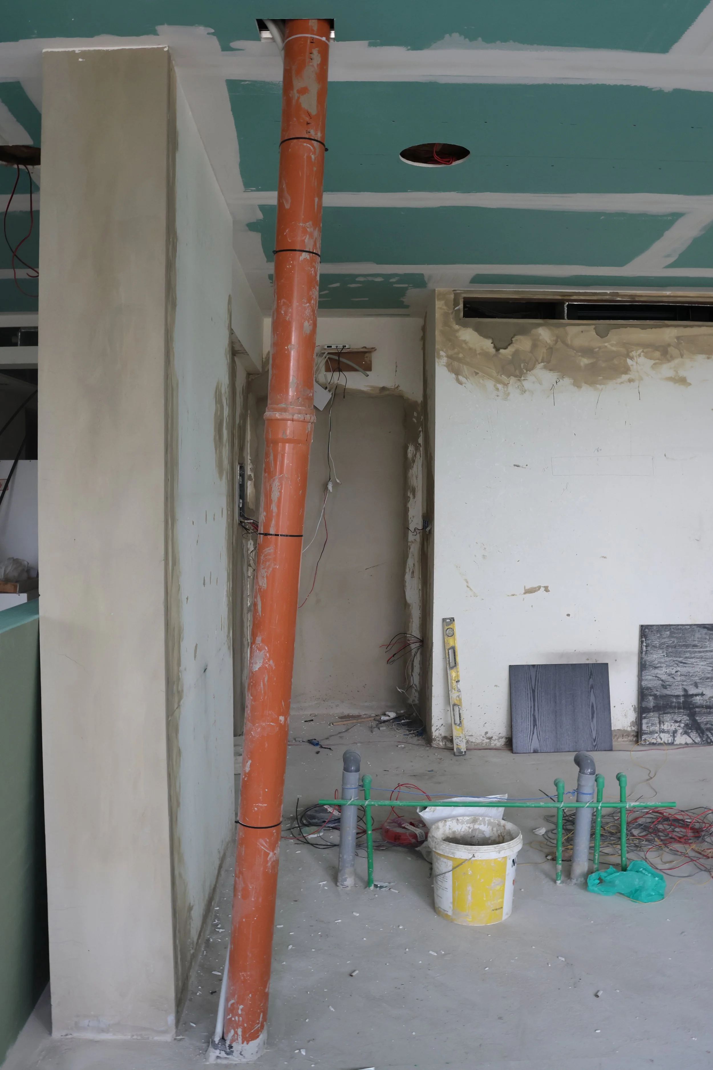 Construction site with exposed pipes, drywall, wiring, and unfinished walls, indicating ongoing interior renovation.