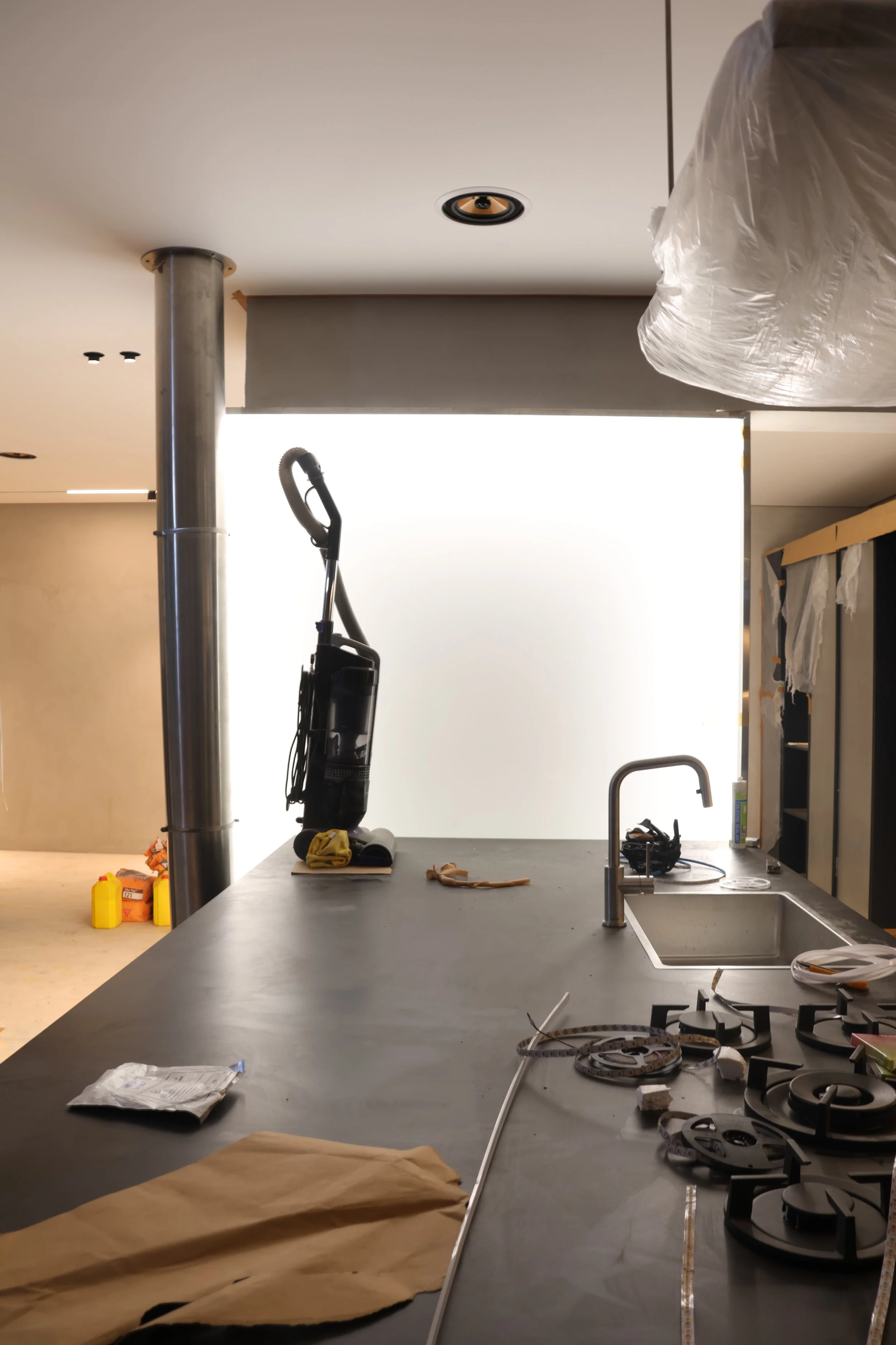 Modern kitchen with a gray countertop, sink, and stove in a space under construction or renovation, with tools and materials scattered.
