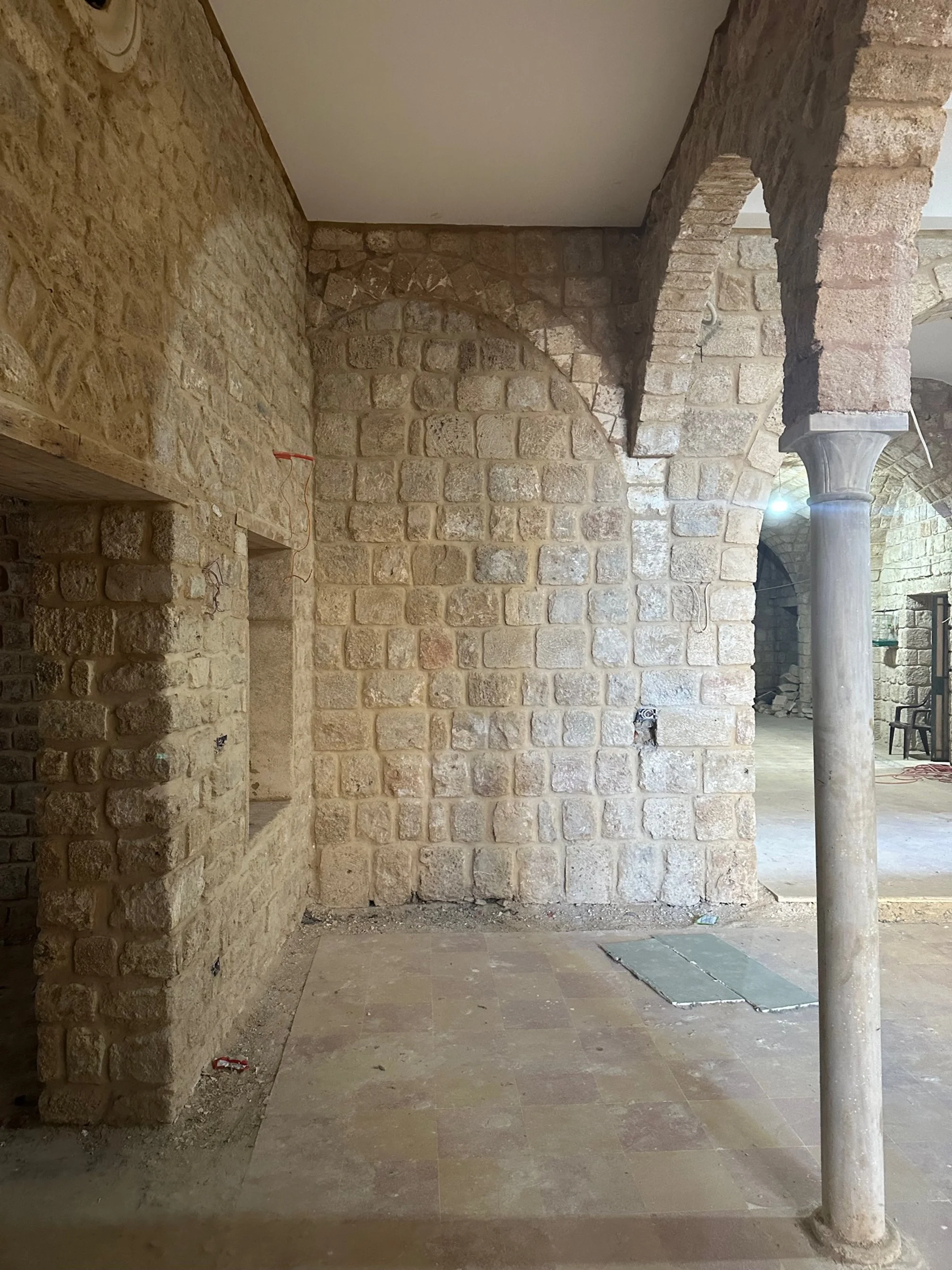 Interior of a building under construction with brick walls, arched doorways, and stone columns.