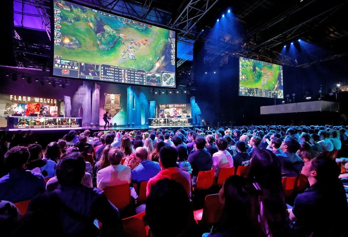 An indoor esports event with a large crowd watching a competitive video game match on big screens, with stage lighting and gaming teams.