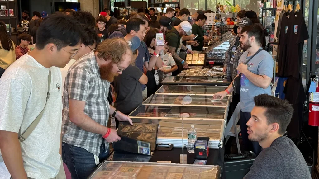People browsing and purchasing collectibles at a convention or comic expo with display cases and merchandise tables.