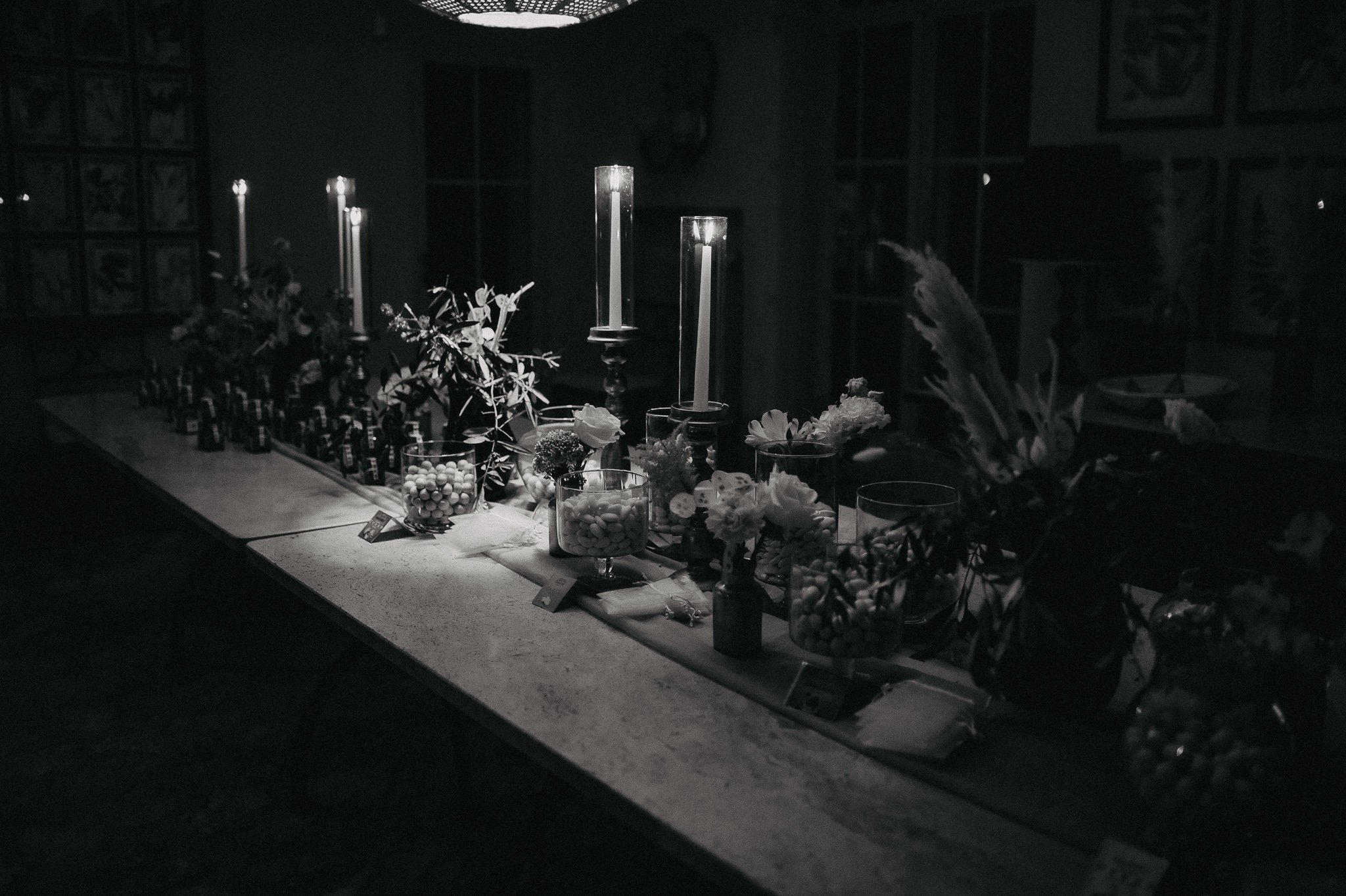 A dimly lit table decorated with flowers, candles, and jars filled with candies, set up for an event.