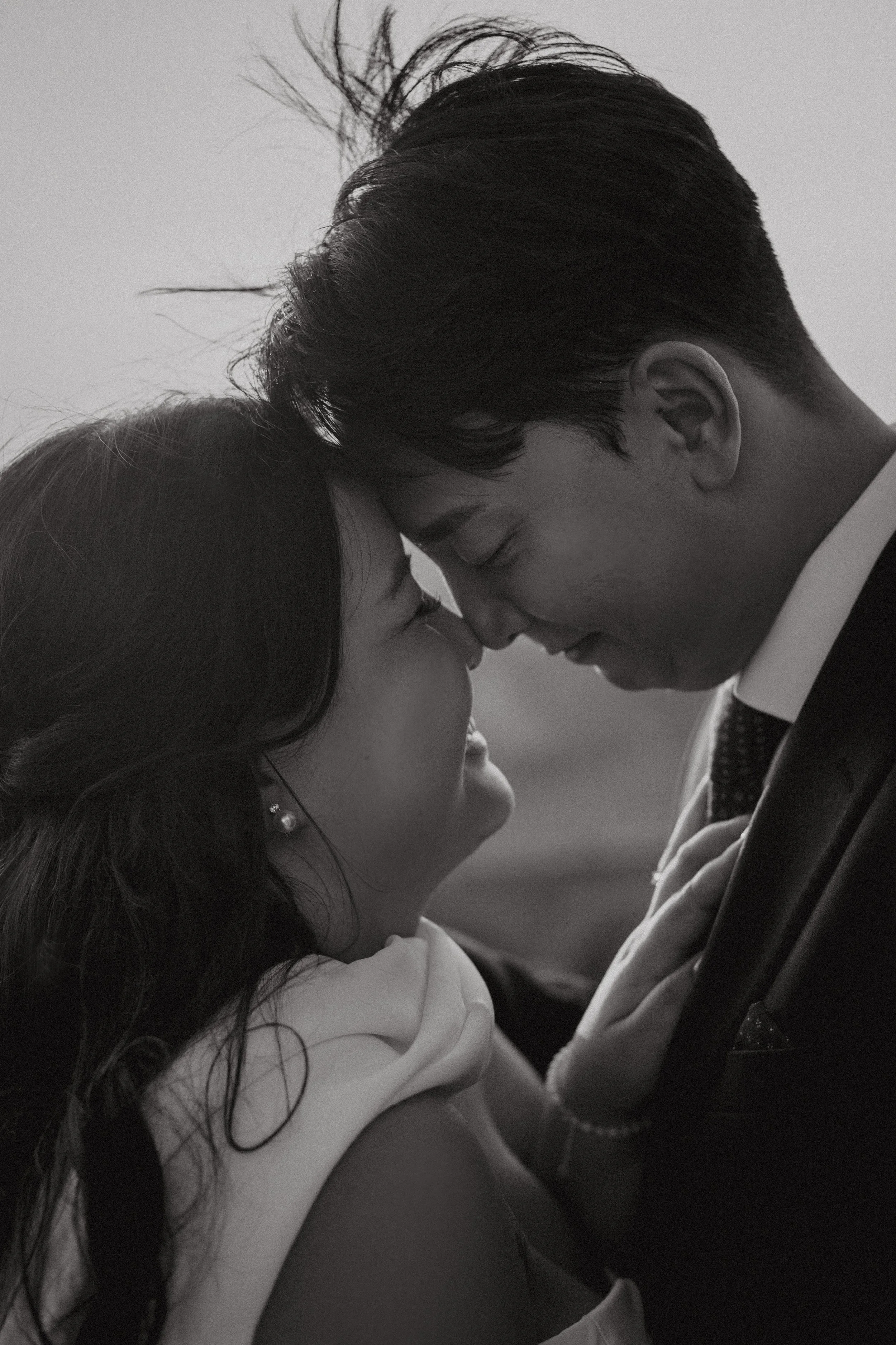 A black and white photo of a couple with foreheads touching, smiling and looking into each other's eyes, in a close, intimate pose.
