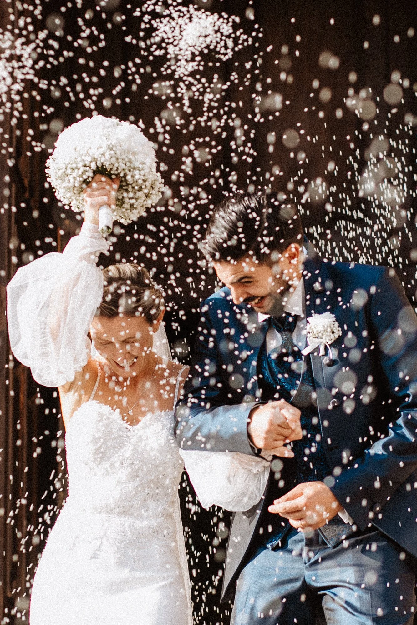 A newlywed couple celebrating with confetti, the bride holding a bouquet and the groom smiling, as they enjoy their wedding celebration.