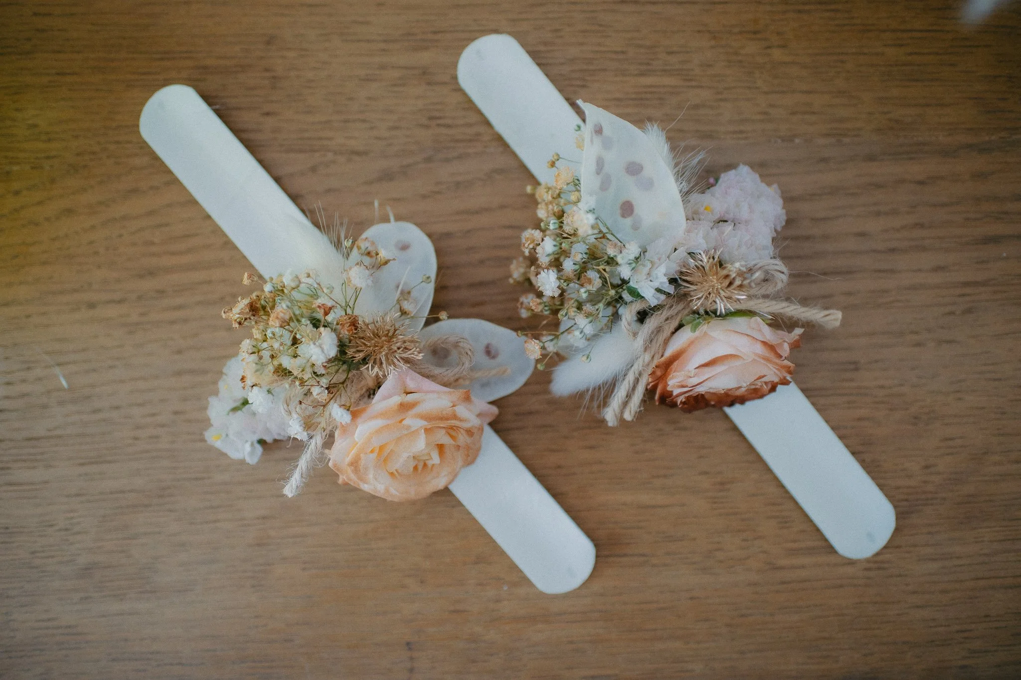 Two white wooden popsicle sticks decorated with flowers, found on a wooden surface.