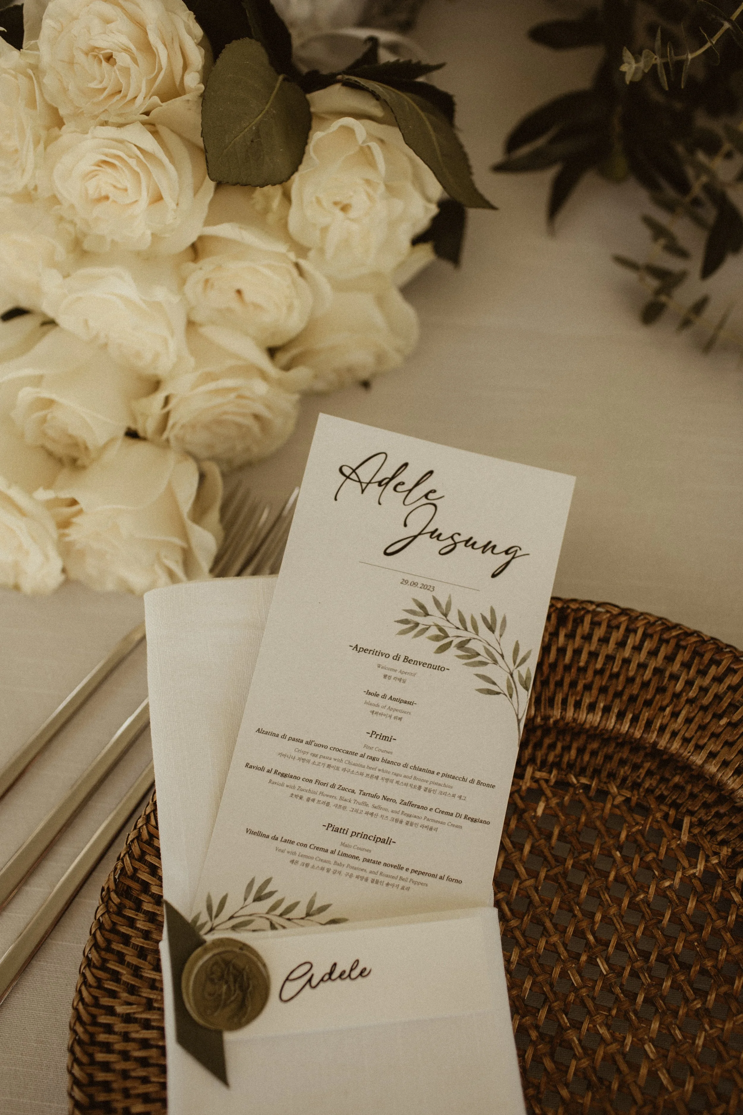 Wedding place card and menu with a bouquet of white roses and green foliage in the background.