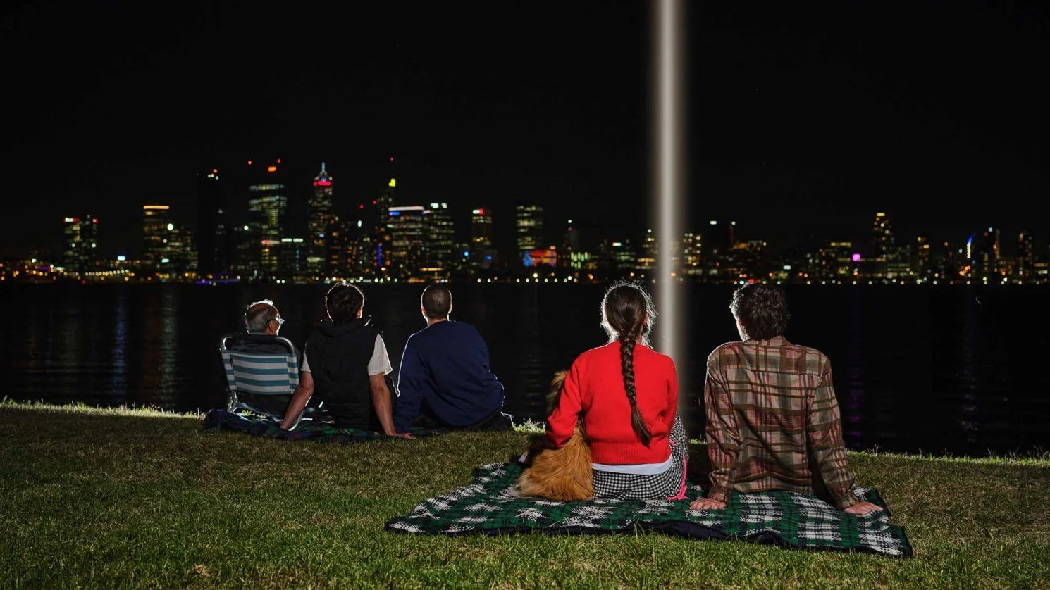 An image of a few people sitting on the foreshore, looking at a beam of light.