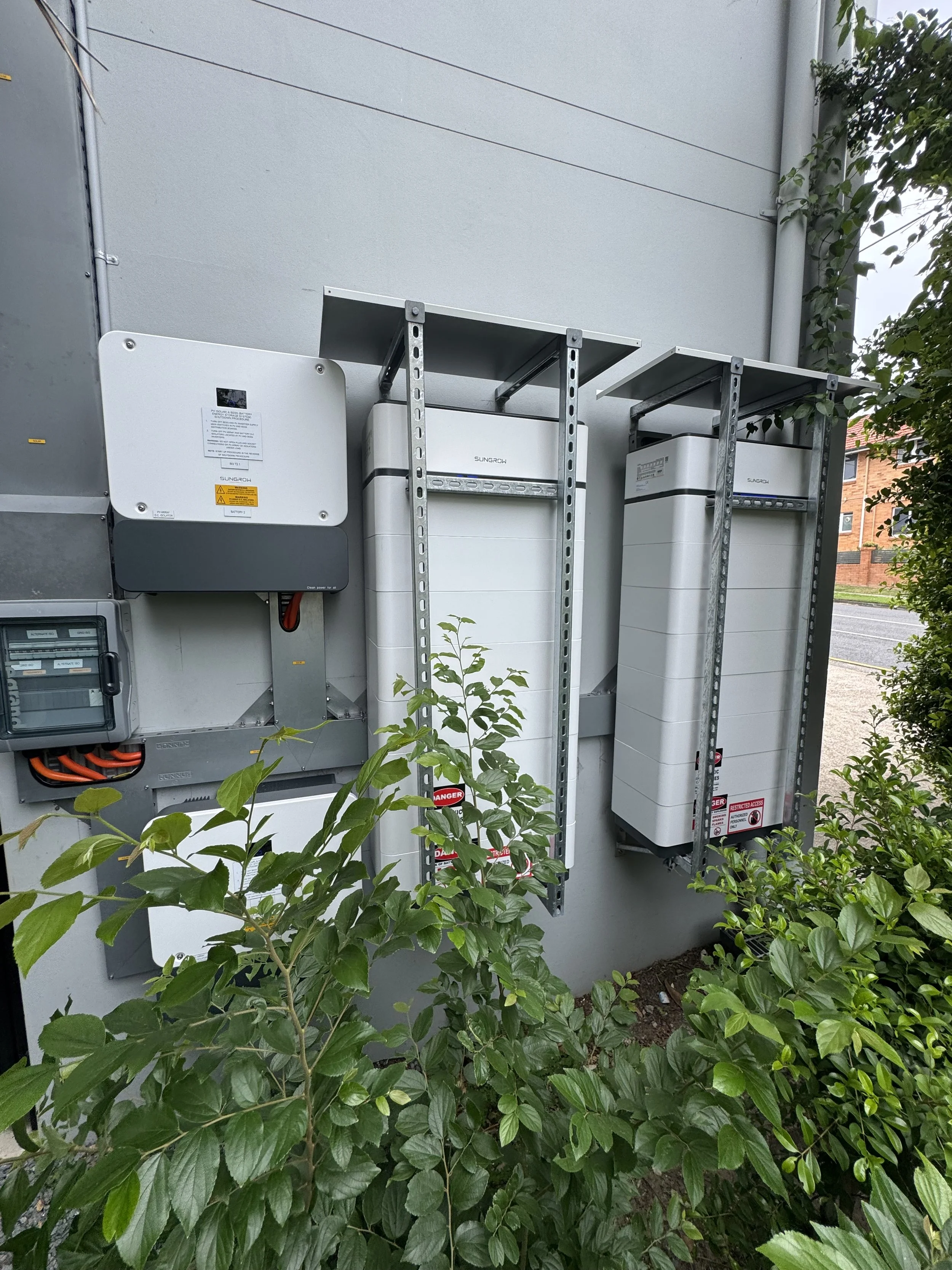 Outdoor electrical equipment with metal framing, surrounded by green bushes and trees.