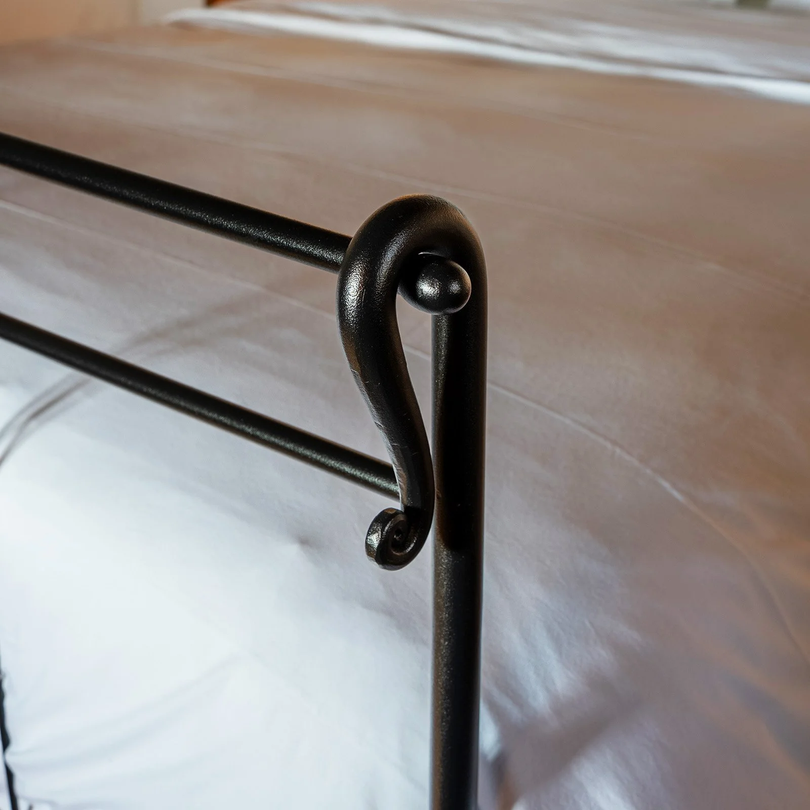 Close-up of a decorative black metal furniture leg with a curl design, supporting a wooden piece, on a white surface.