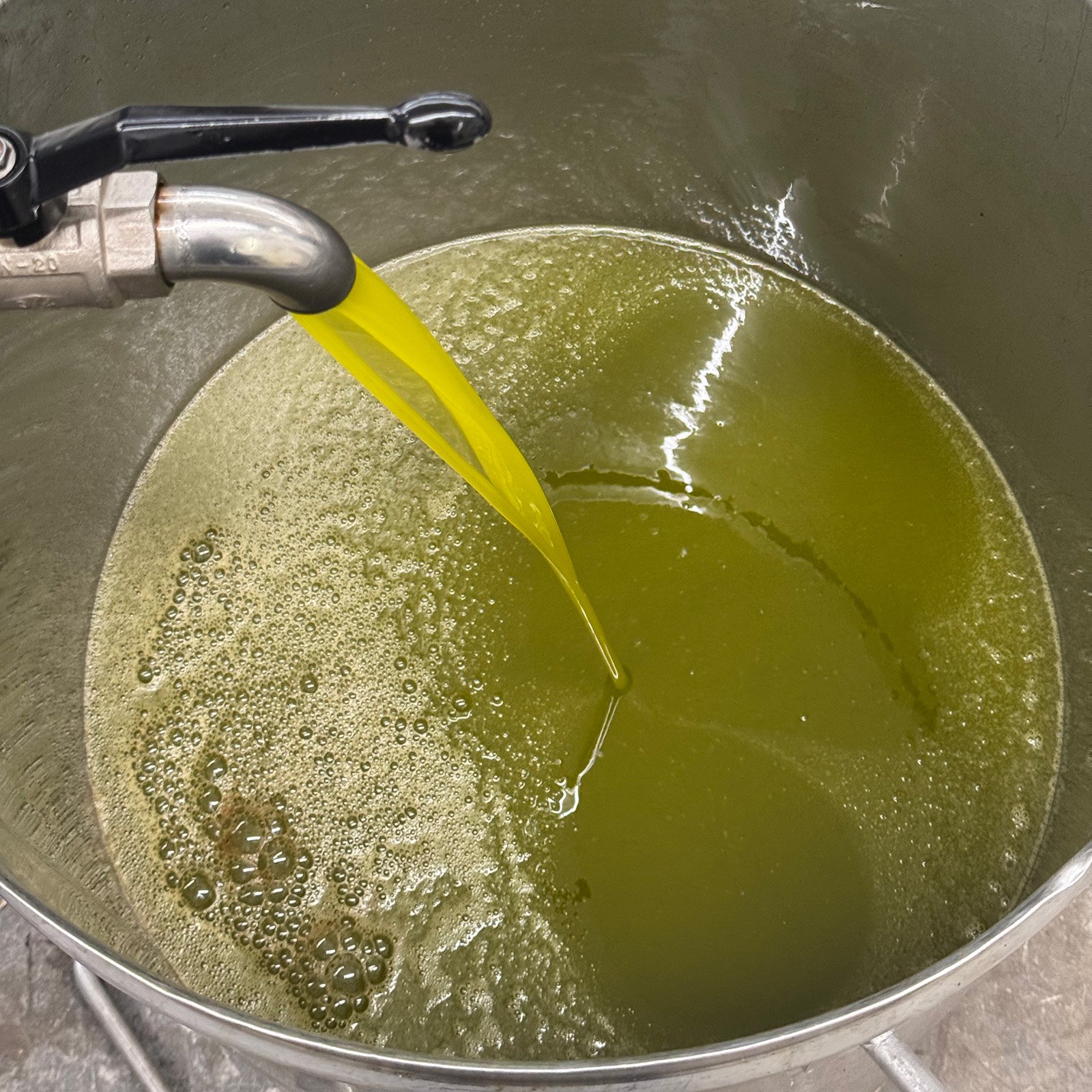 Greenish liquid being poured into a metal container from a tap.