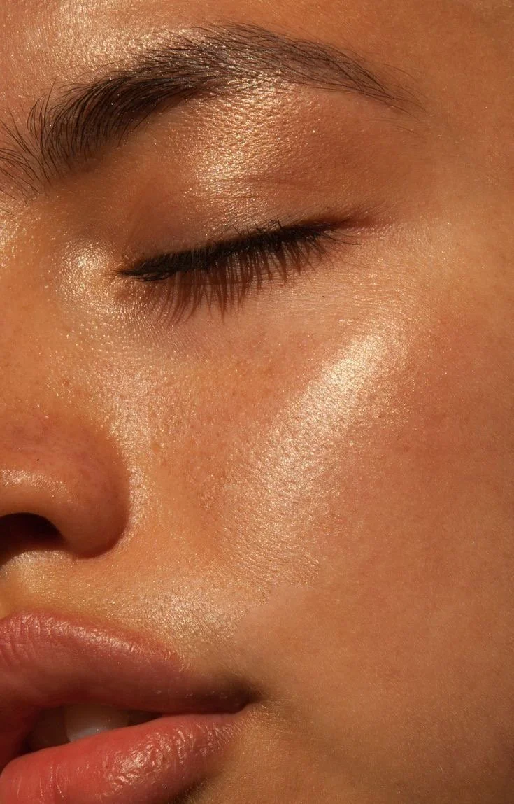 Close-up d'un visage avec la peau éclatante, des sourcils bien définis, un œil fermé, et des lèvres légèrement entrouvertes.