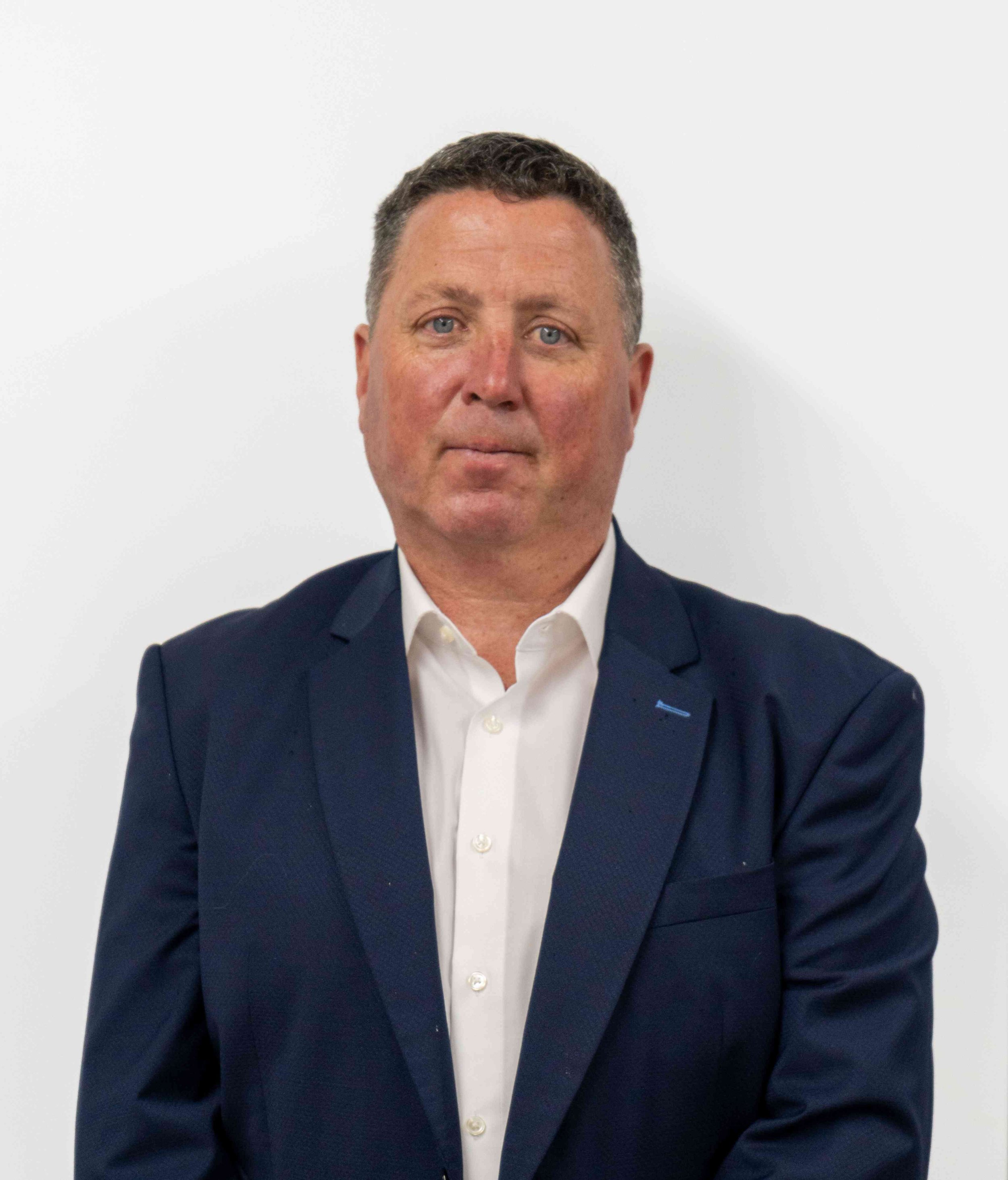 A man in a navy blue suit with a white dress shirt, posing against a plain white background.