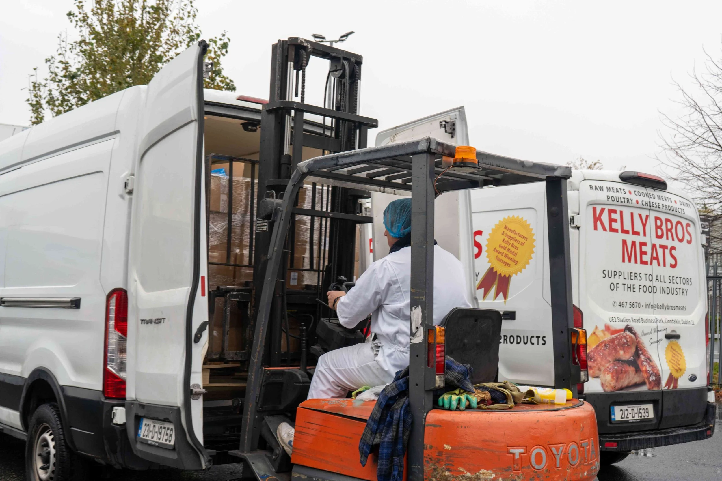 Worker operating a forklift on a Kelly Bros Meats delivery truck filled with boxed meat products.