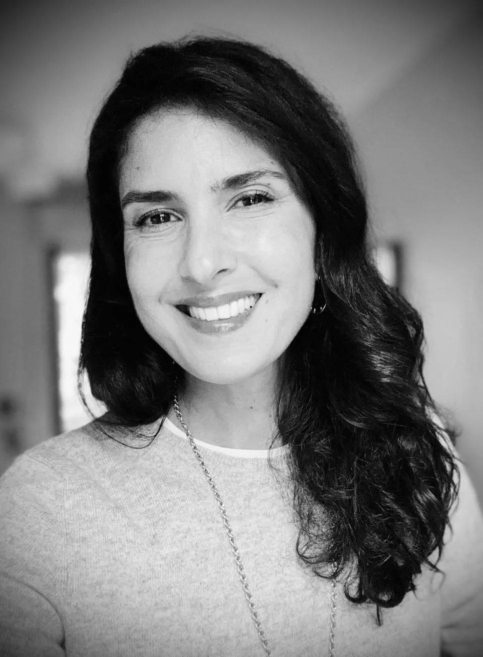 Portrait en noir et blanc d'une femme souriante avec des cheveux longs et ondulés.