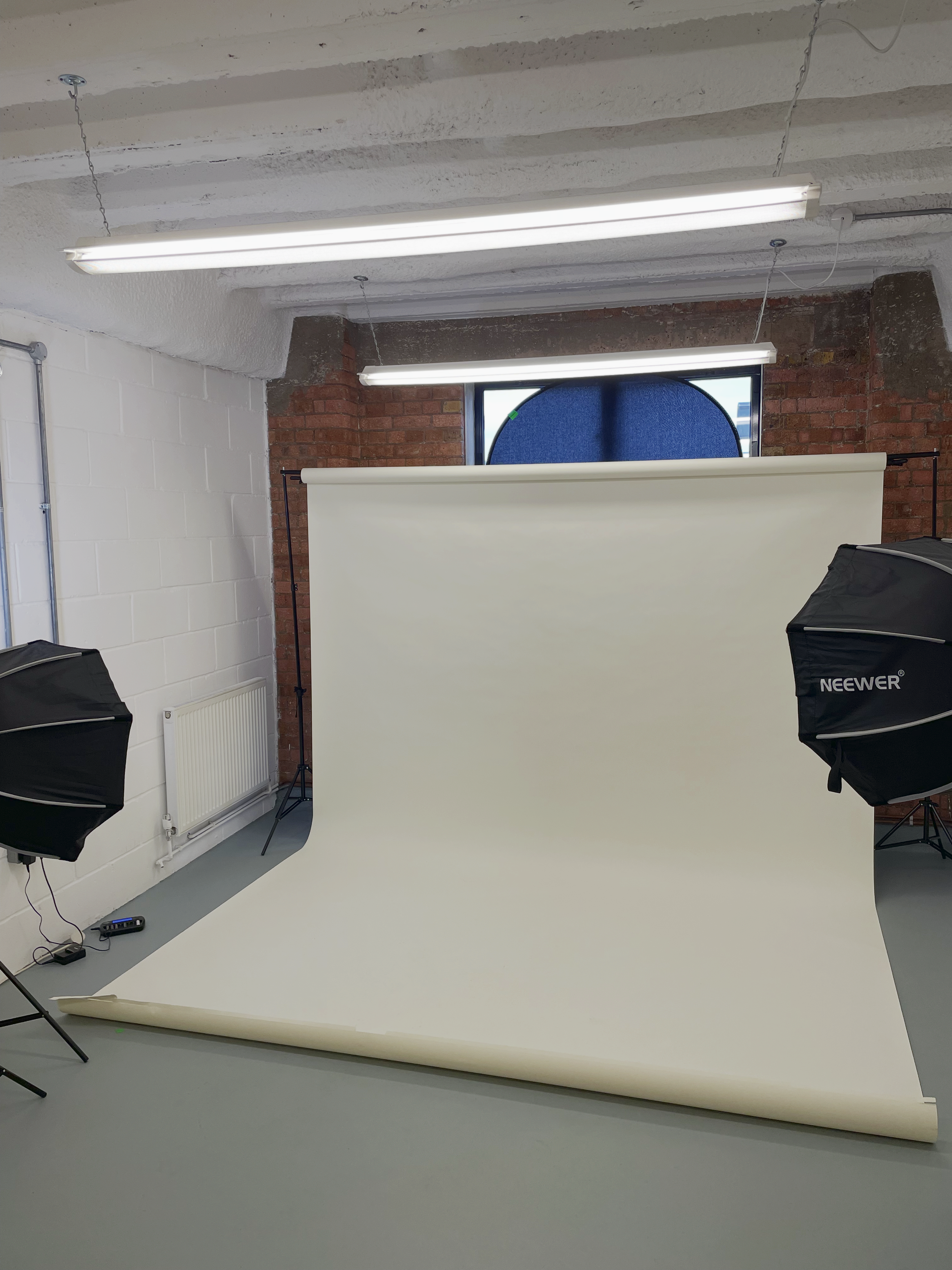 Photography studio with white backdrop, two softbox lights, a blue circular prop in the window, in a room with brick and white walls.