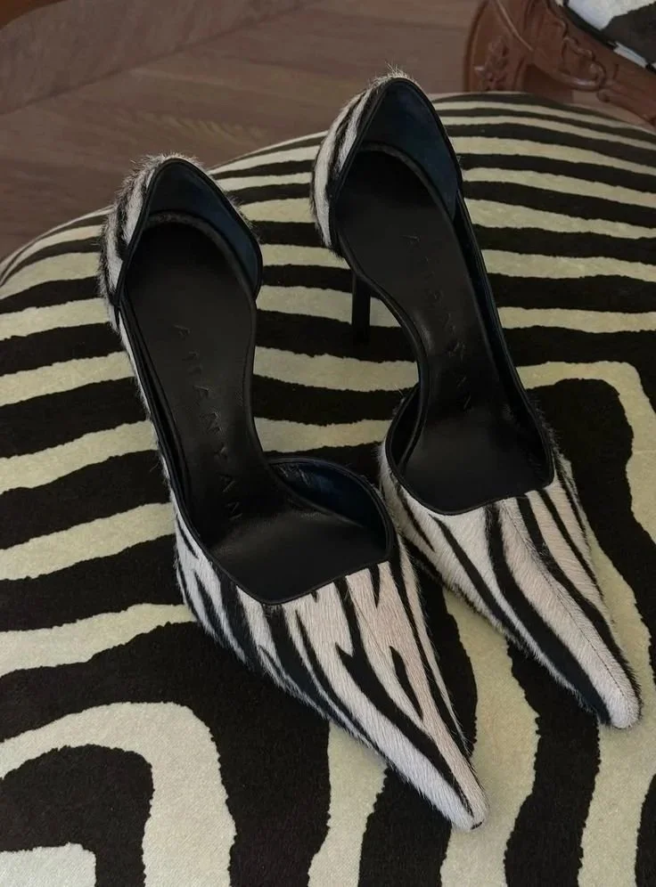 Pair of high-heeled shoes with black and white zebra print pattern, placed on a matching zebra print rug.