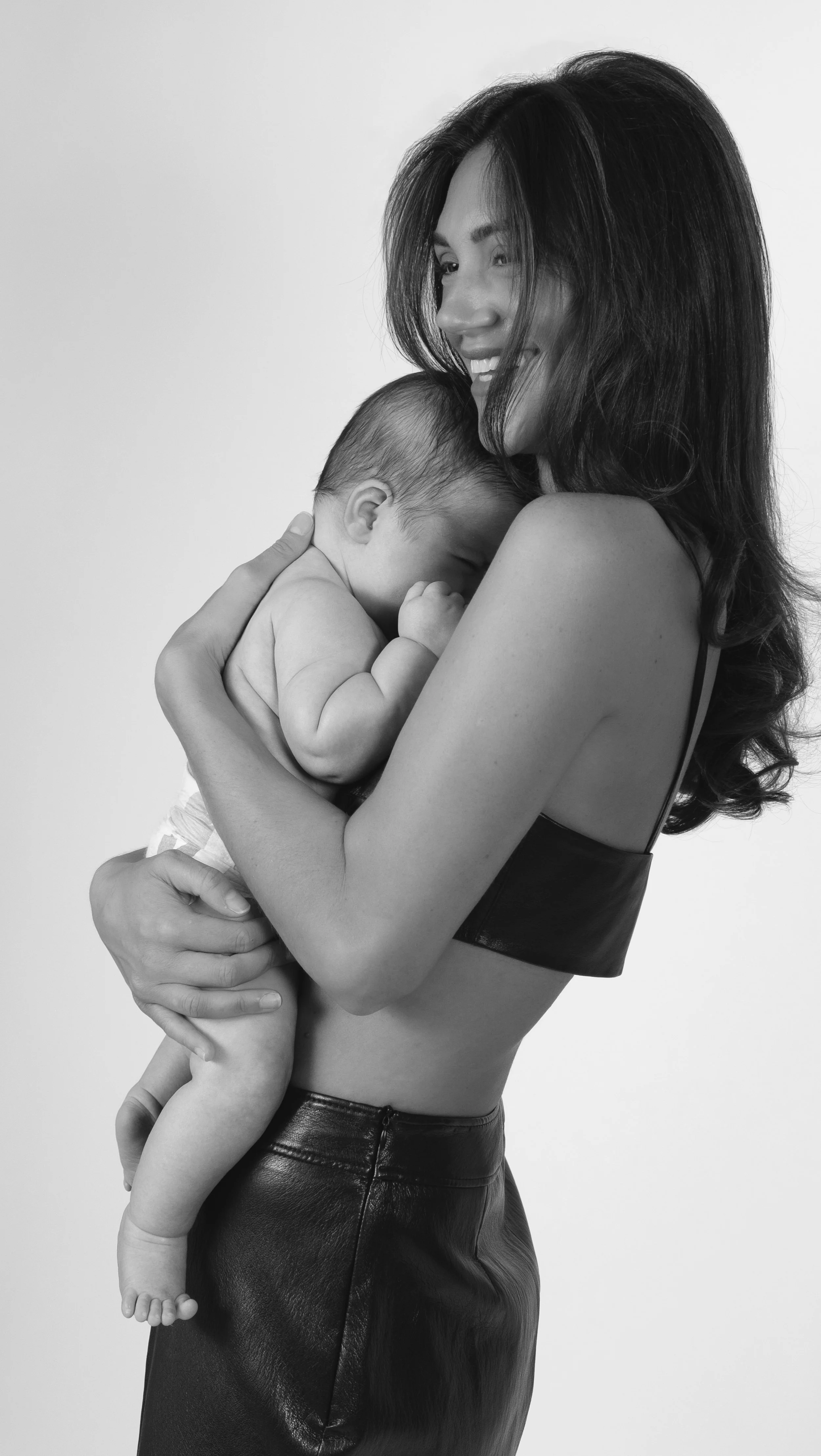 A woman holding a sleeping baby close to her chest, smiling, in black and white.