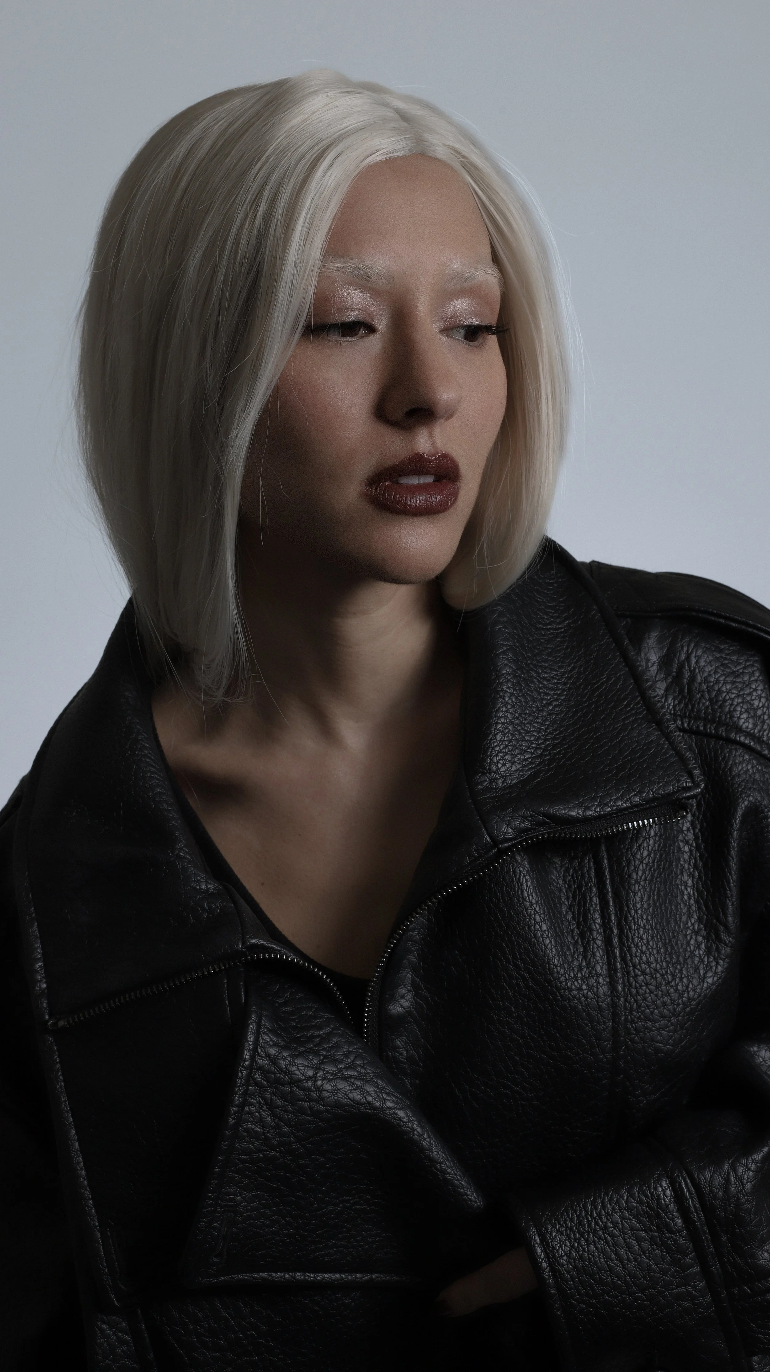 A woman with platinum blonde hair wearing a black leather jacket against a plain background.