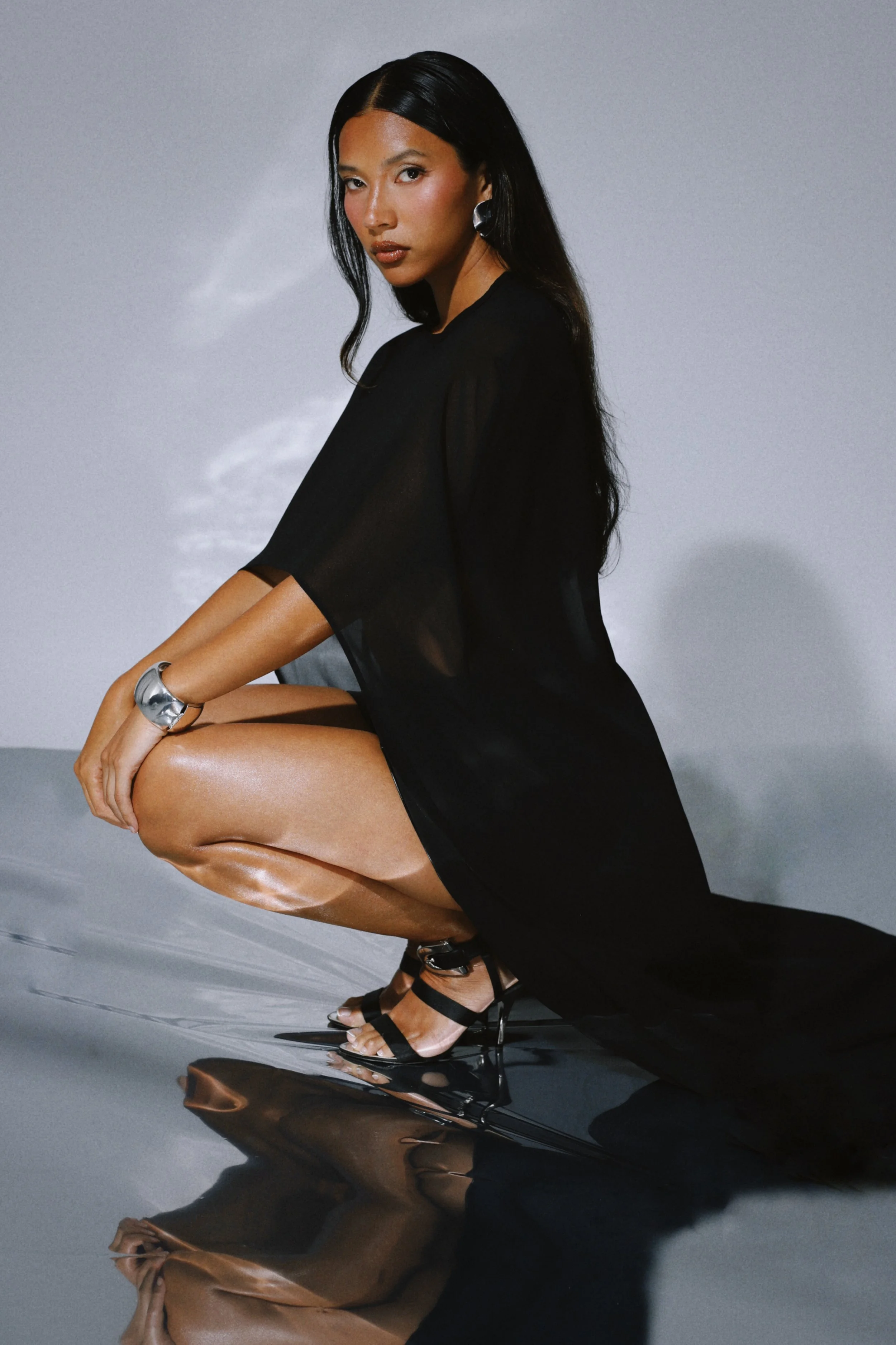 Model crouched in the black sheer dress, side angle, looking toward camera.