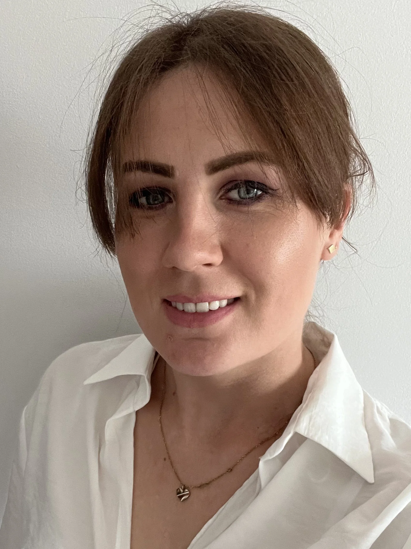 Smiling woman with shoulder-length black hair wearing a blue top, standing in a lush green indoor garden.