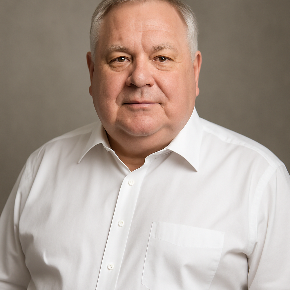 A portrait of a young man with brown hair, wearing a gray sweater over a collared shirt, smiling softly against a plain gray background.