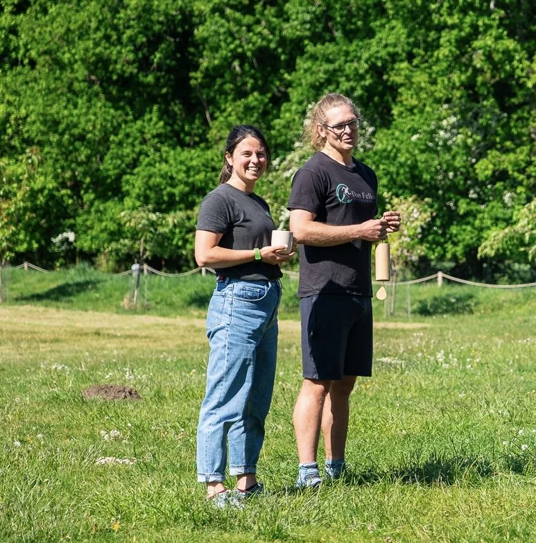 Jeni and Dan standing outside with trees and green grass in the background. 