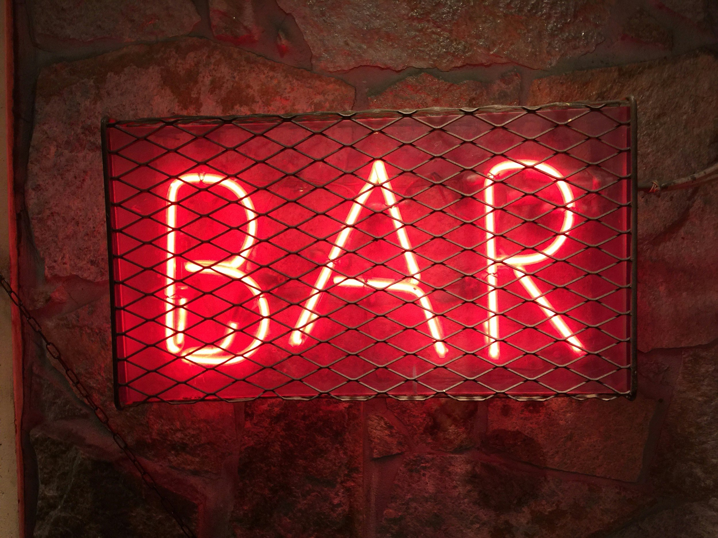 A red neon sign with the word 'BAR' illuminated behind a black metal grid.