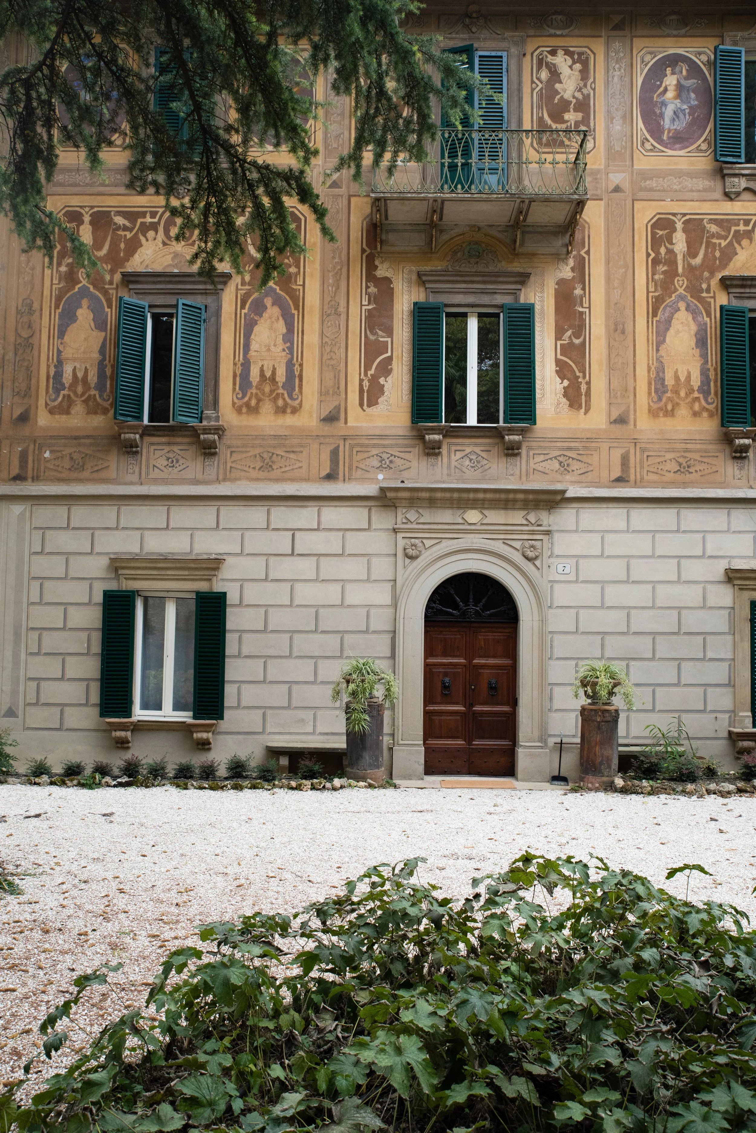Paesaggio montano con montagne innevate sullo sfondo e colline verdi e secche in primo piano, con alcuni edifici in mezzo.