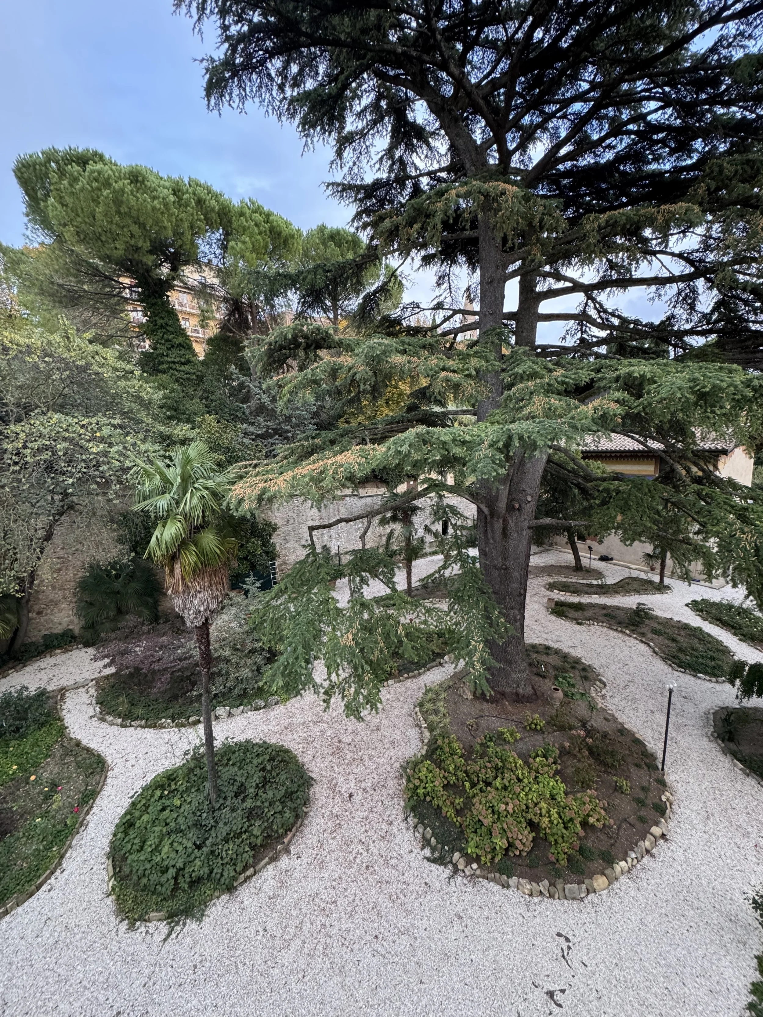 Giardino con percorsi di ghiaia, alberi e piante ornamentali.